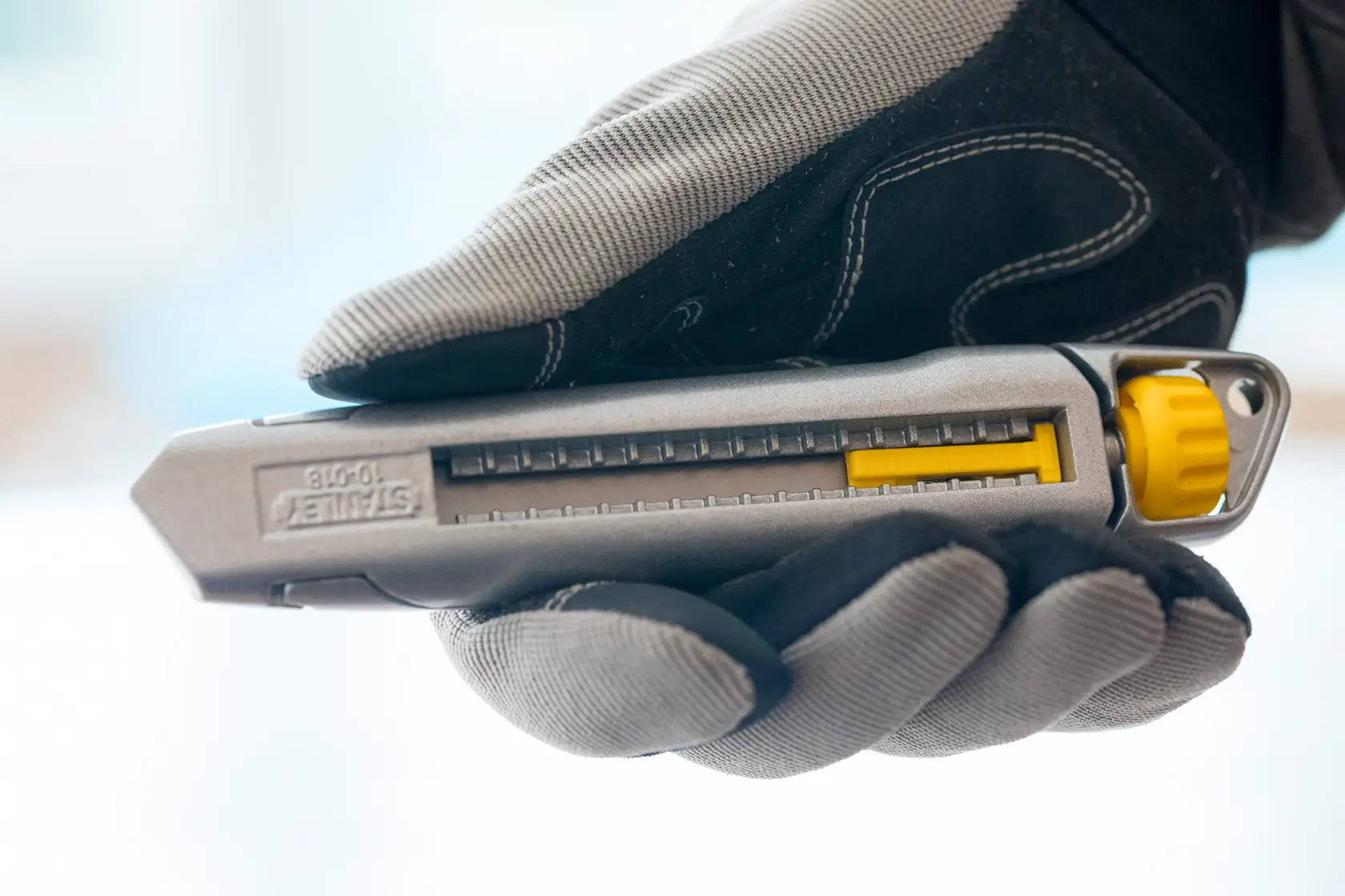 Photo of STANLEY 0-10-018 utility knife with gray and yellow design, held in a gloved hand, side view.