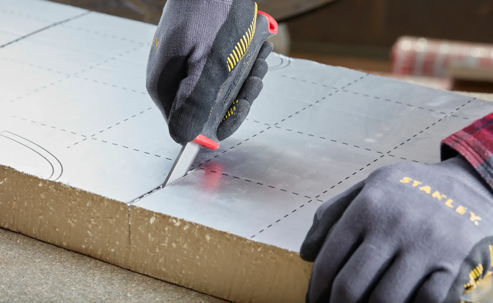 Photo of STANLEY 0-10-231 utility knife cutting foil-faced insulation board, close-up angle, hands wearing gloves.