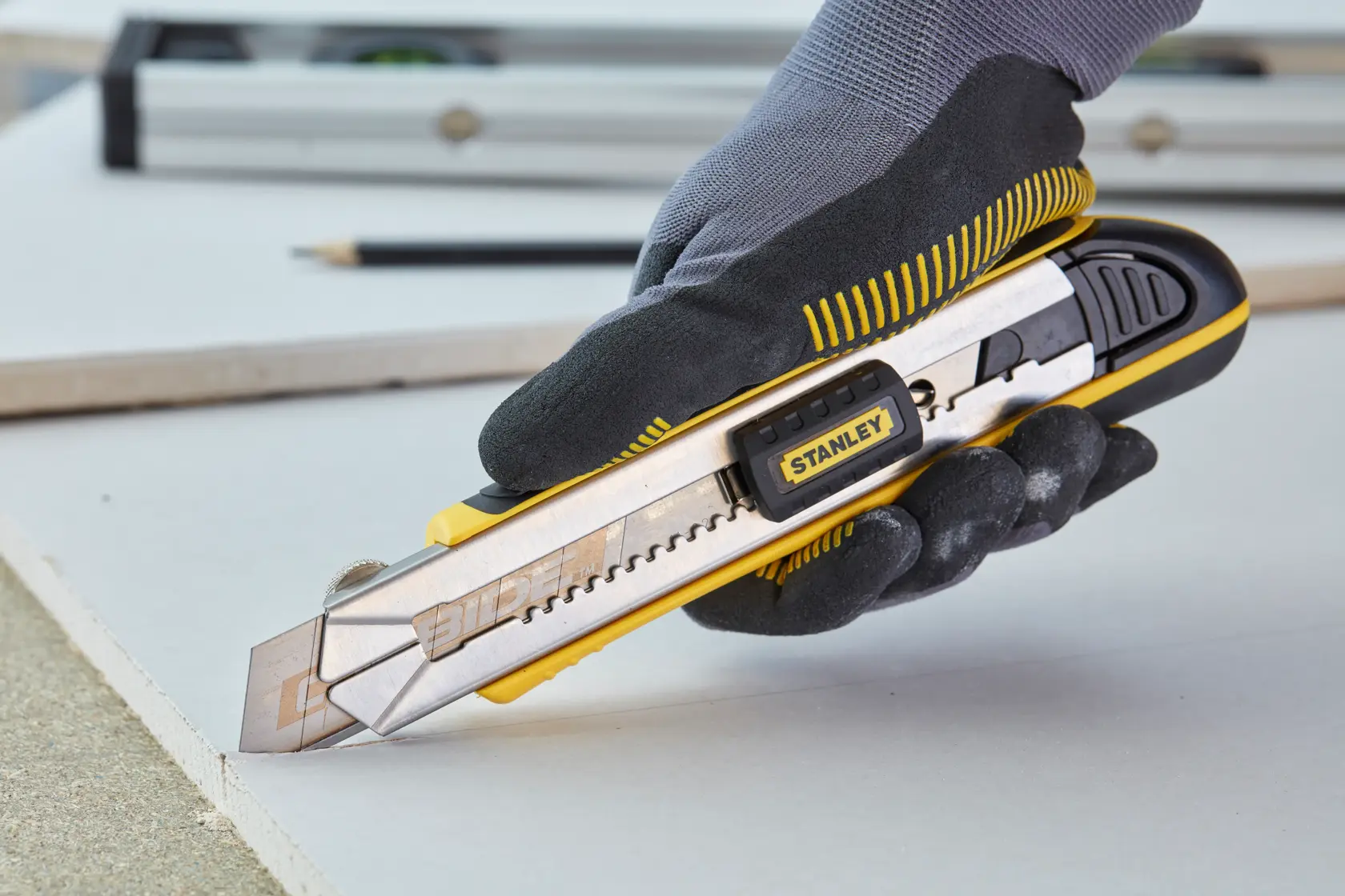 STANLEY 0-10-481 utility knife cutting drywall, ergonomic handle, silver and yellow finish, close-up side view.