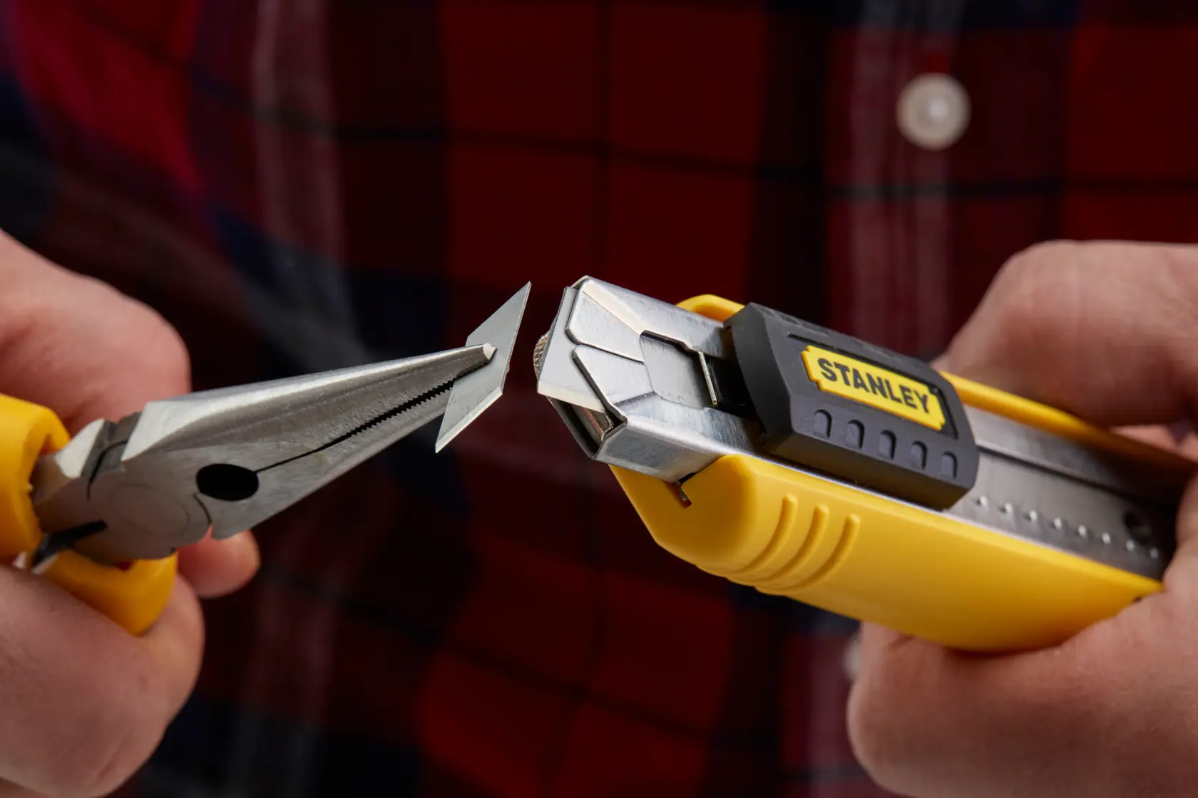 Photo of STANLEY 0-10-481 utility knife with yellow handle, blade held by pliers, close-up in use.