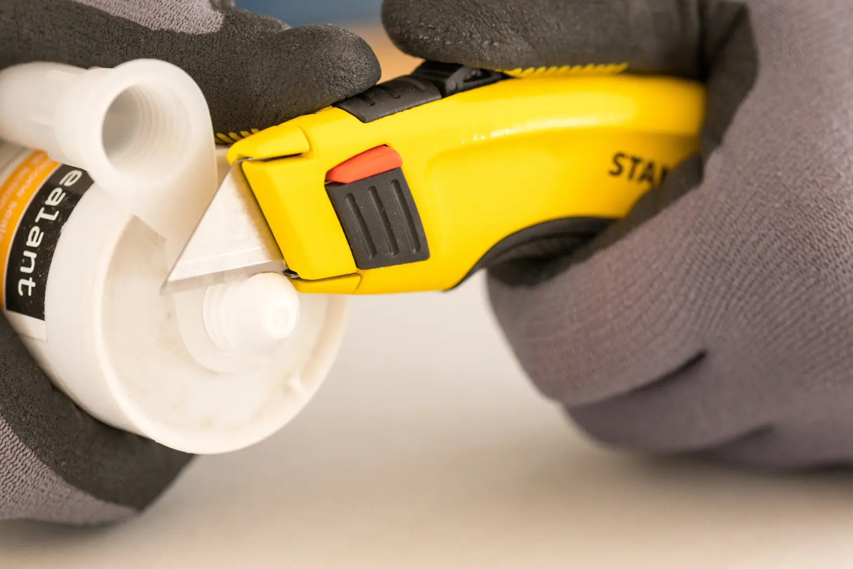 Photo of STANLEY 0-10-778 utility knife cutting plastic tube, close-up view, hands in gloves holding both items.