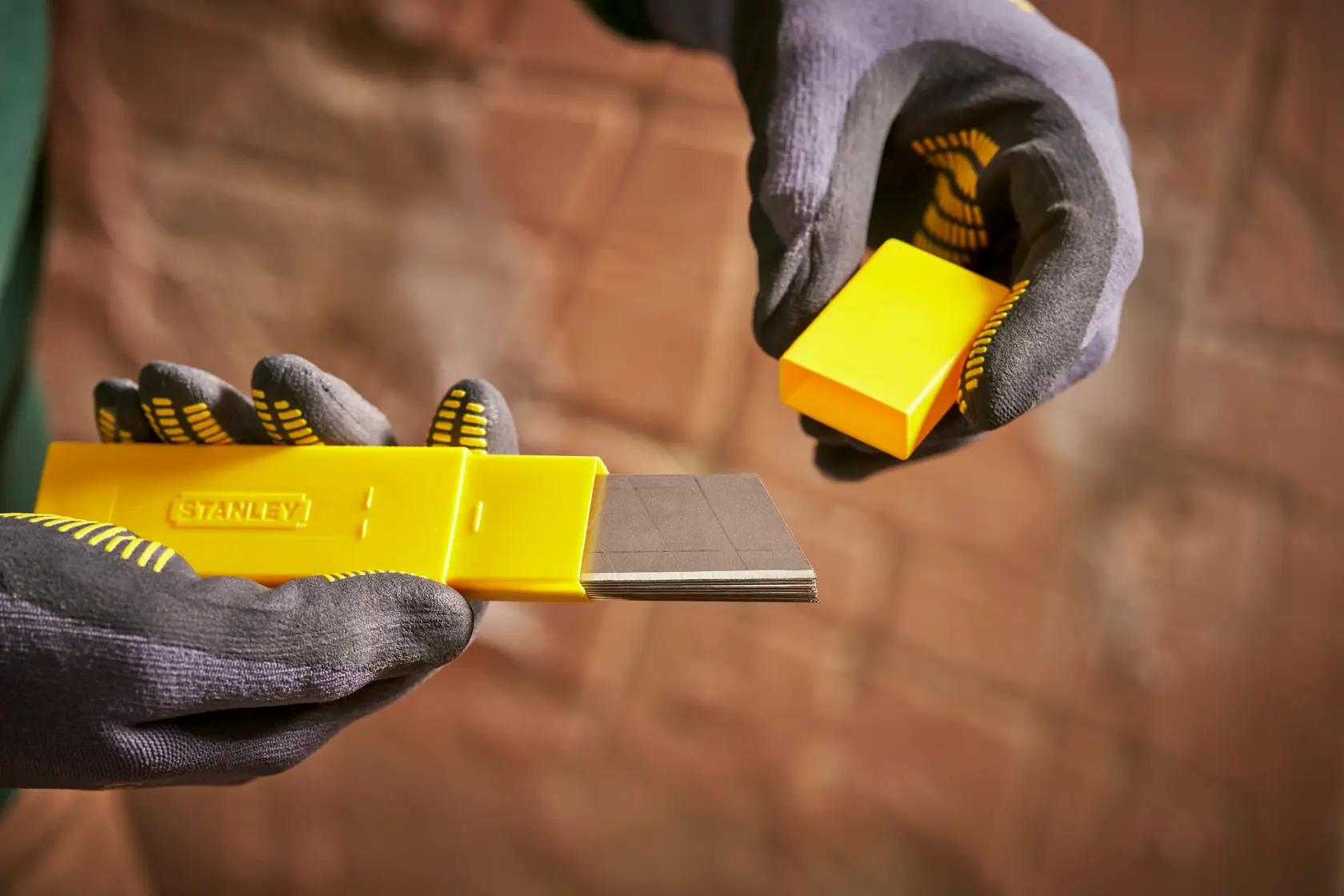 STANLEY 0-11-325 yellow blade dispenser held in gloved hands, showing multiple utility blades.