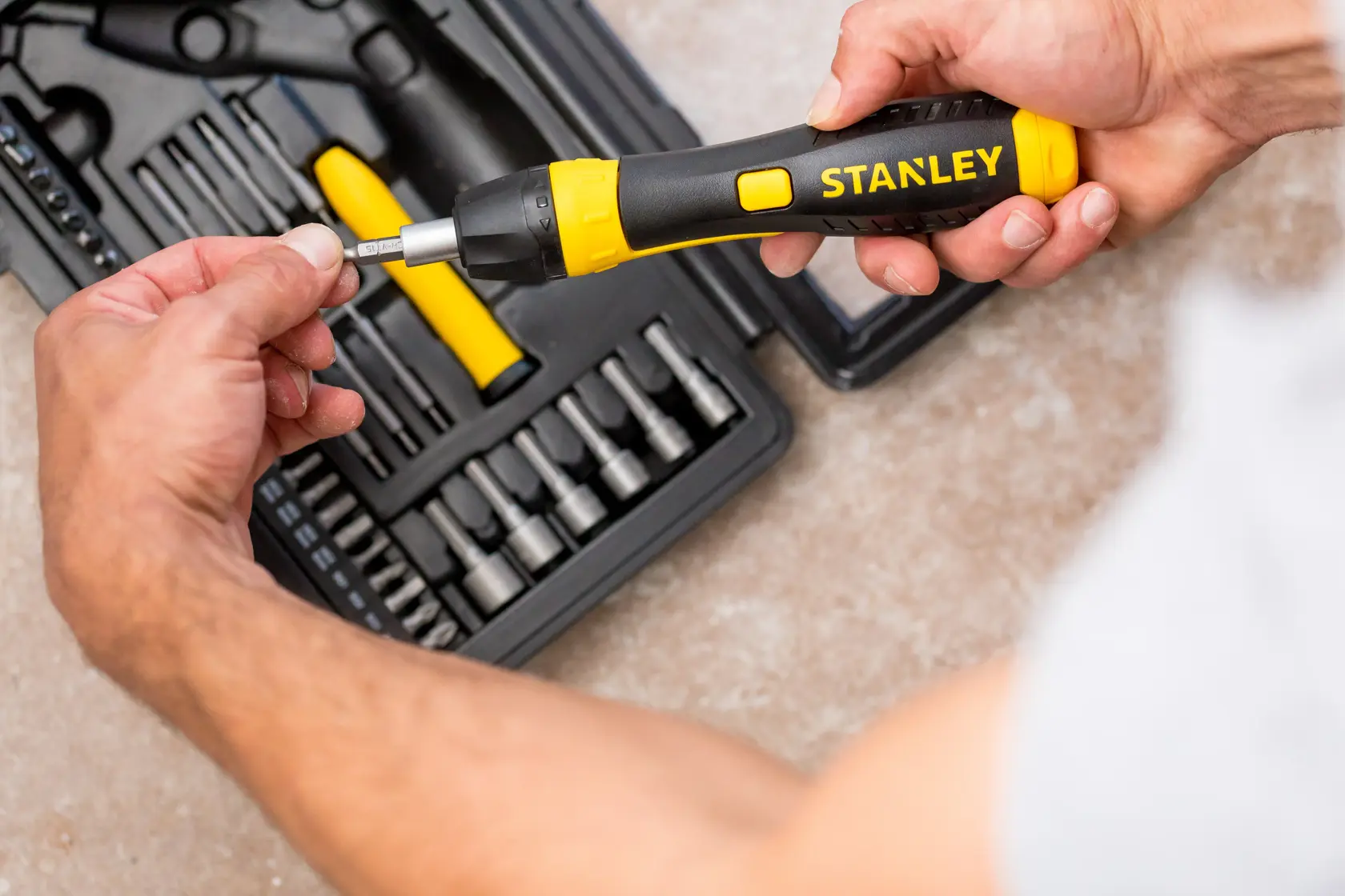 STANLEY 0-63-038 ratcheting screwdriver set with black and yellow handle, person inserting bit, top view.