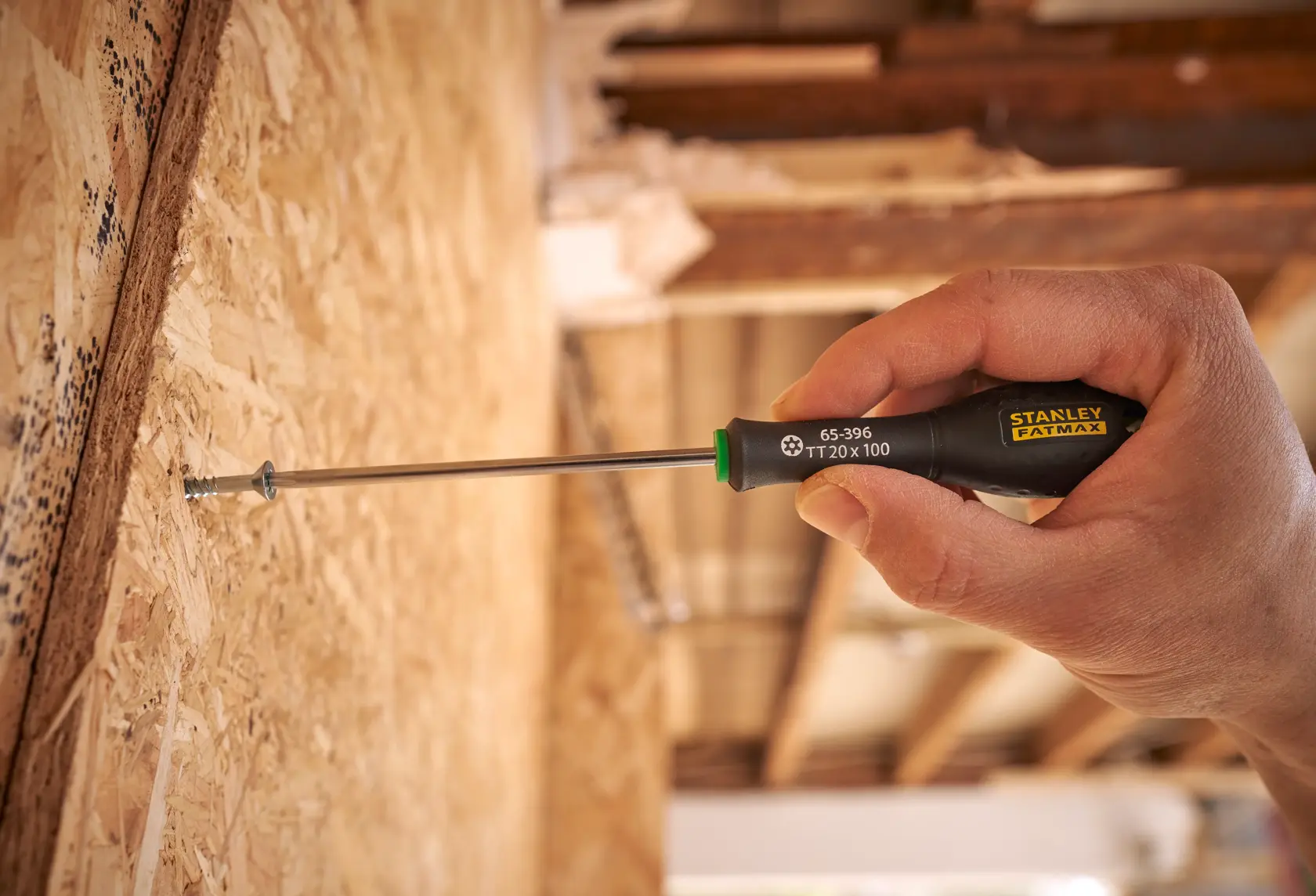 Stanley 0-65-396 screwdriver in use, black handle with yellow logo, tightening screw into wood surface.