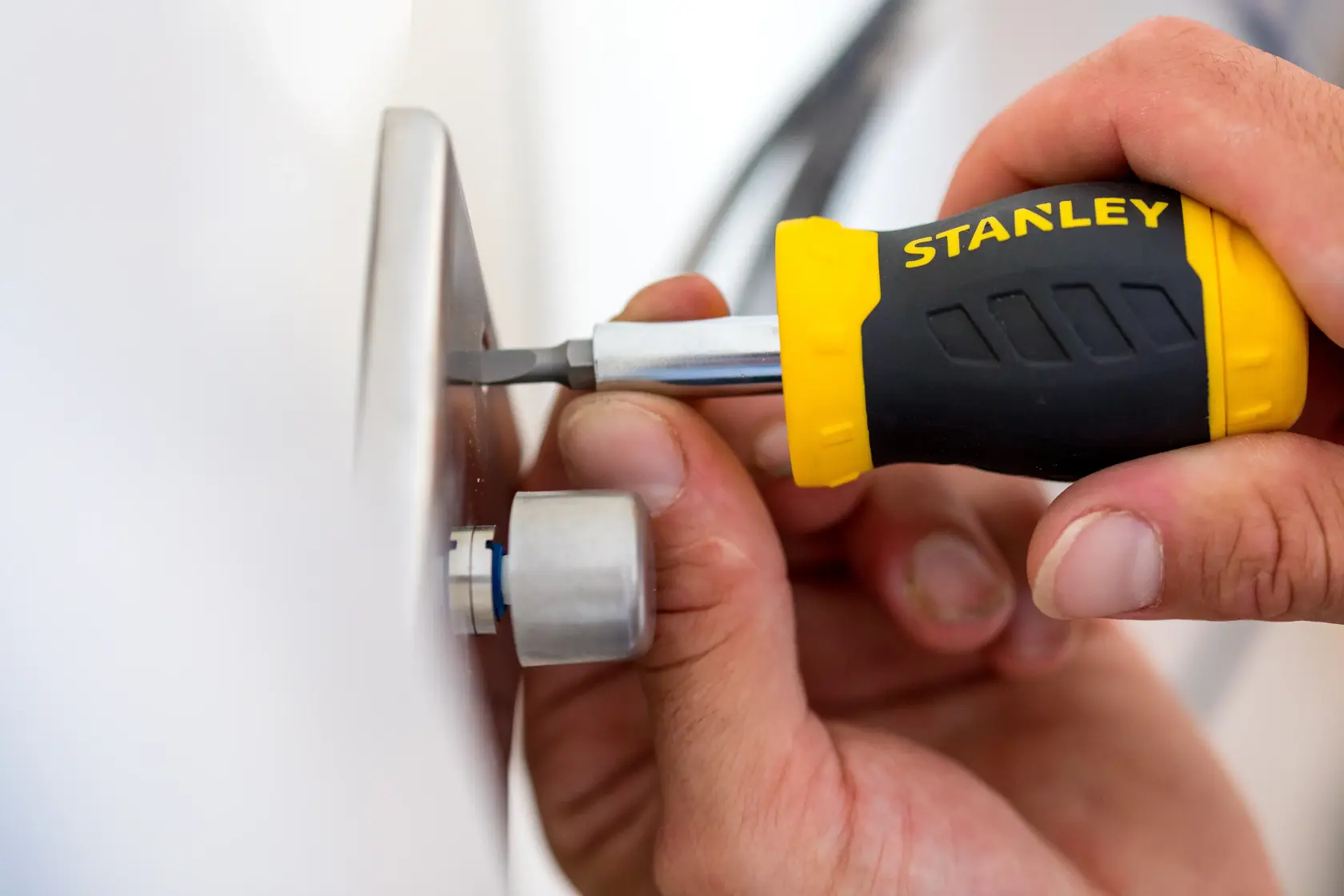 STANLEY 0-66-357 screwdriver with yellow and black handle used to tighten a screw on a metal plate.