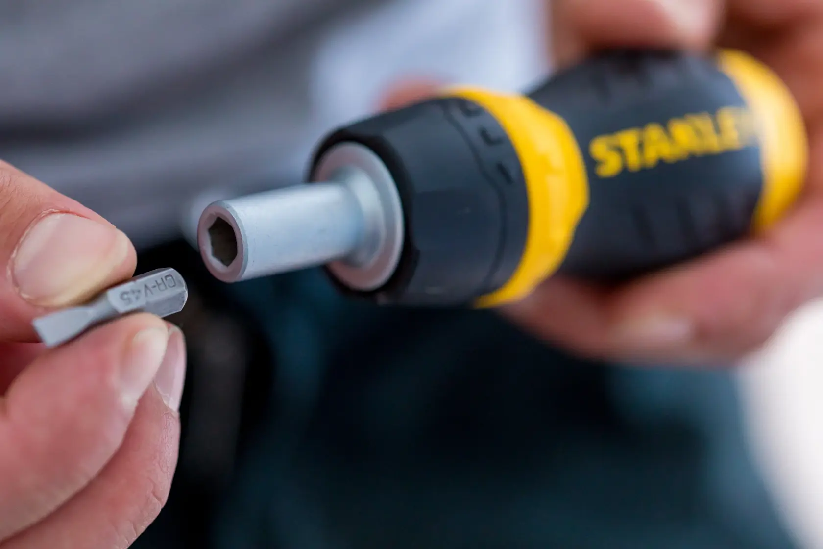 Stanley 0-66-358 screwdriver handle with yellow and black grip, user inserting bit, close-up photo.
