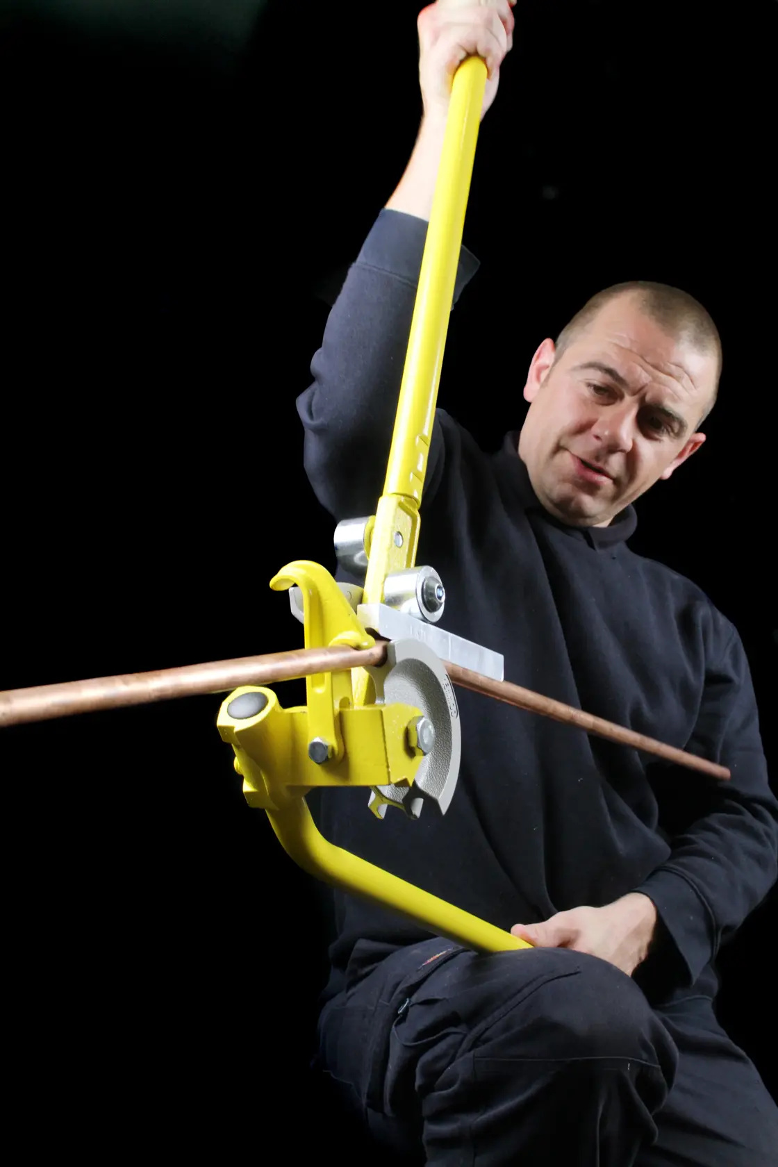 STANLEY 0-70-452 manual pipe bender in use bending a copper pipe, shown against a dark background.