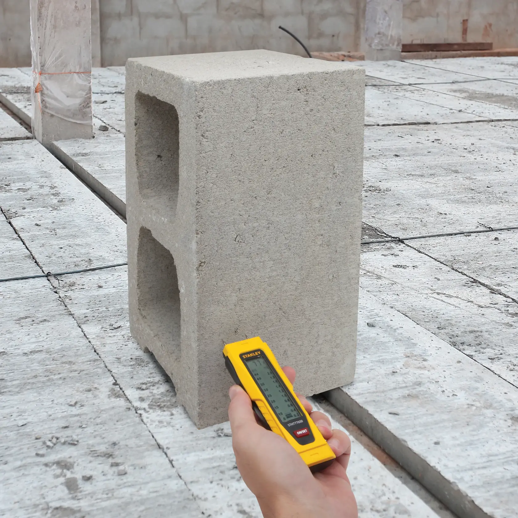 STANLEY 0-77-030 laser distance meter held with yellow casing near cinder block on construction site.