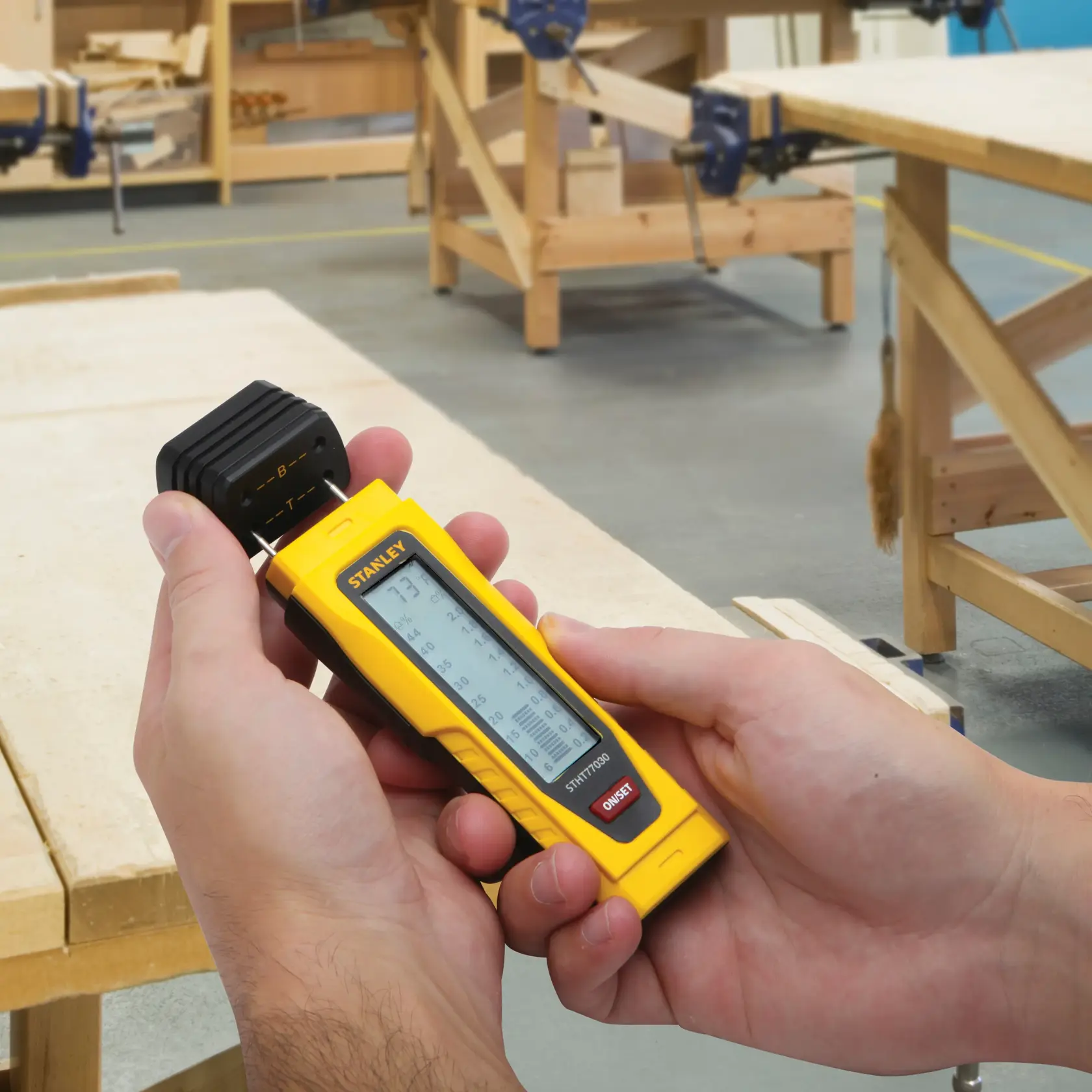 Photo of STANLEY 0-77-030 digital moisture meter held in hands in a woodworking workshop.