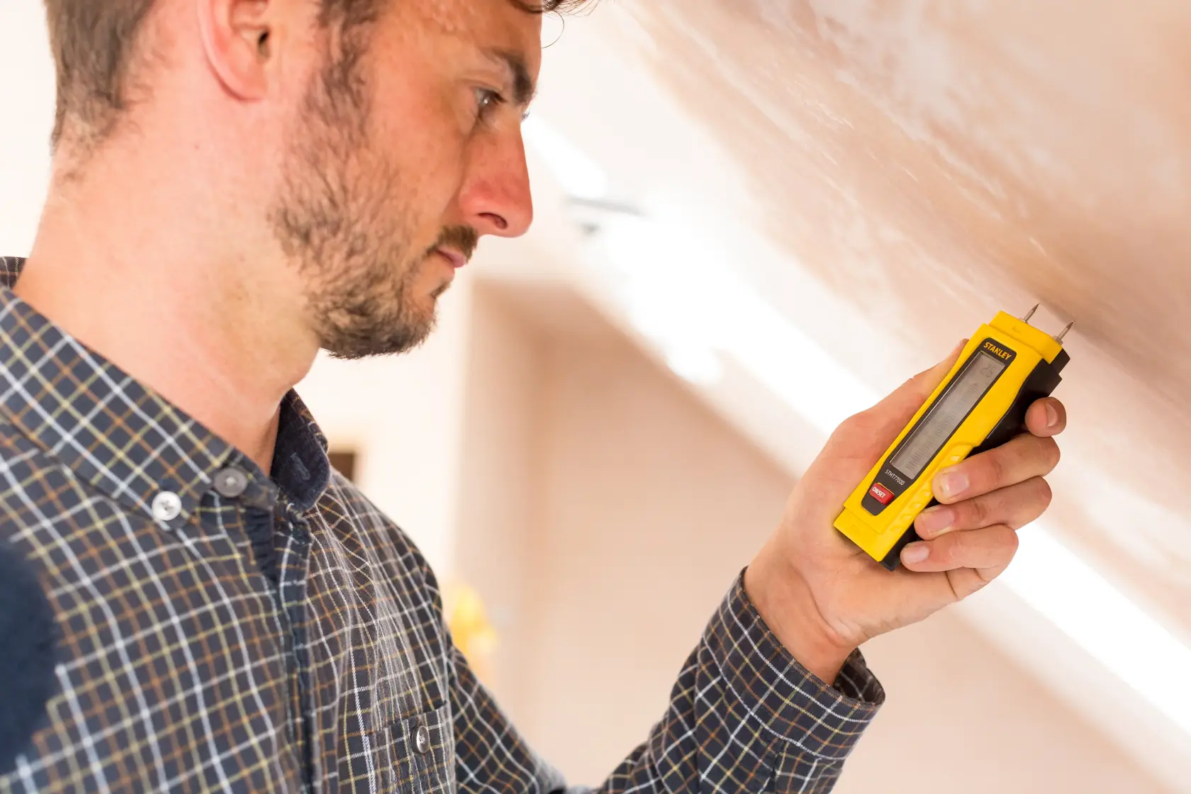 STANLEY 0-77-030 moisture meter used by person against wall, yellow handheld tool, product in use.