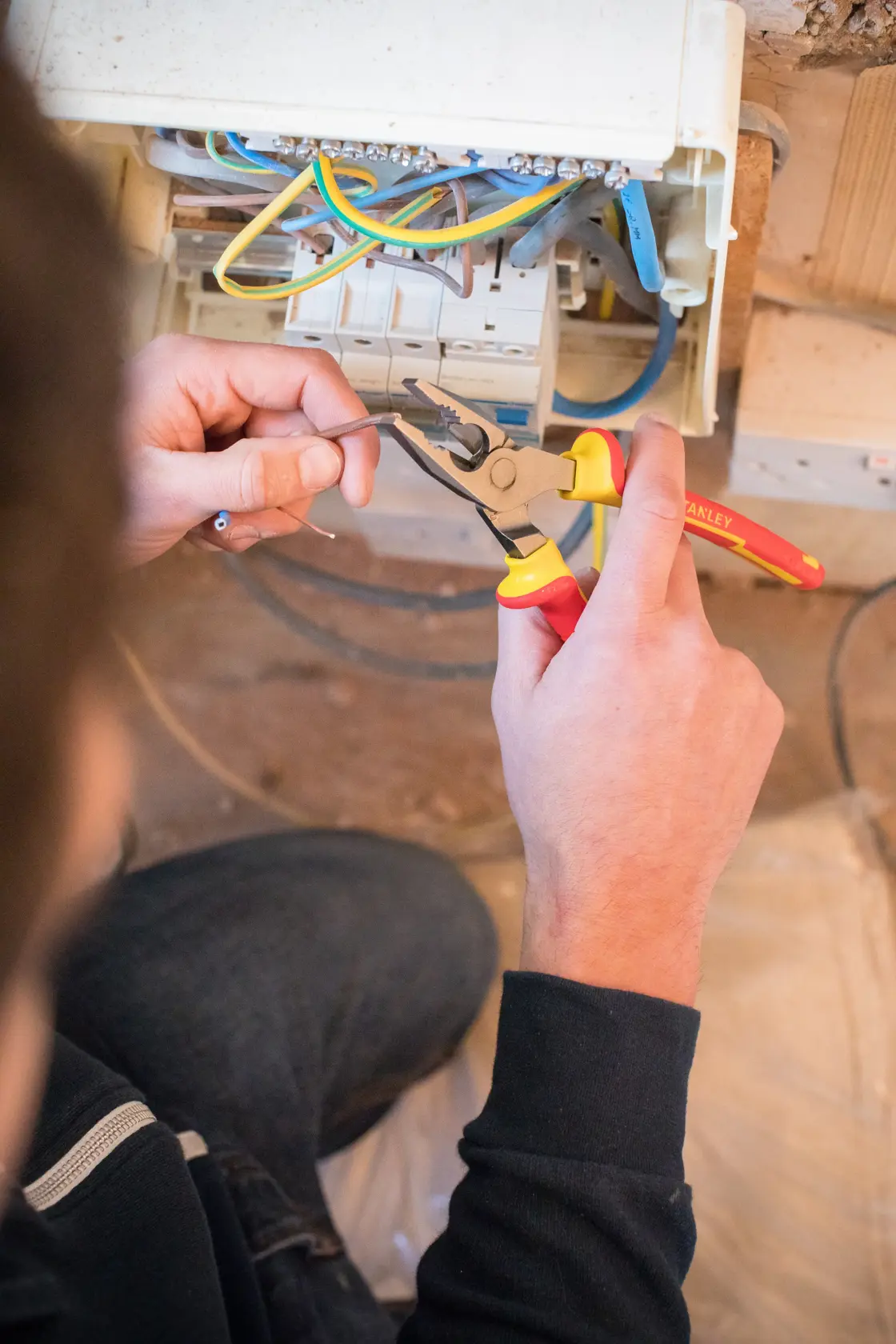 Photo of STANLEY 0-84-001 pliers being used to cut wire during electrical work near a fuse box.