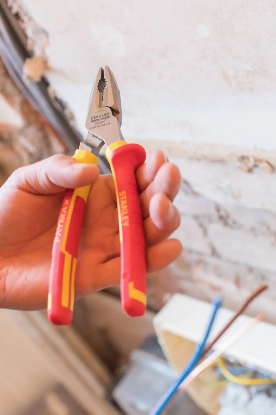 STANLEY 0-84-001 insulated pliers with red and yellow handles, held in hand near exposed wiring.