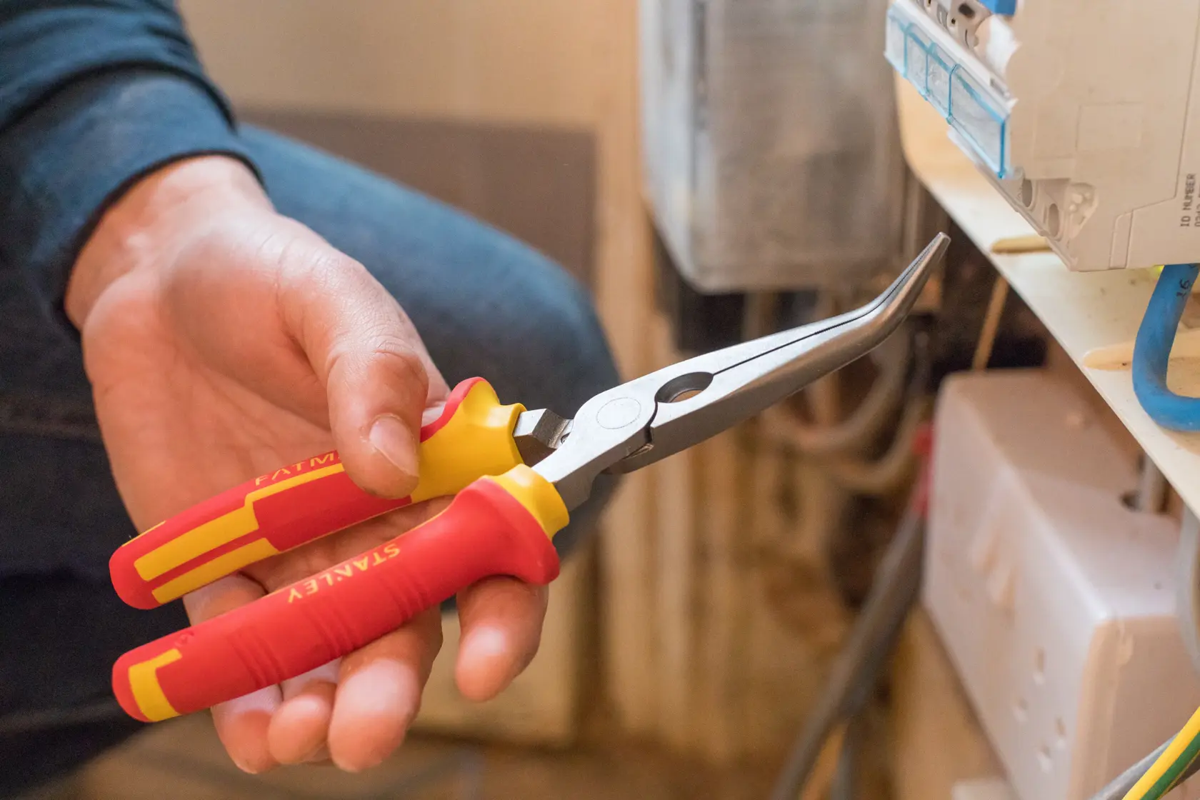 STANLEY 0-84-008 insulated bent long nose pliers in hand, red and yellow handle, close-up view.