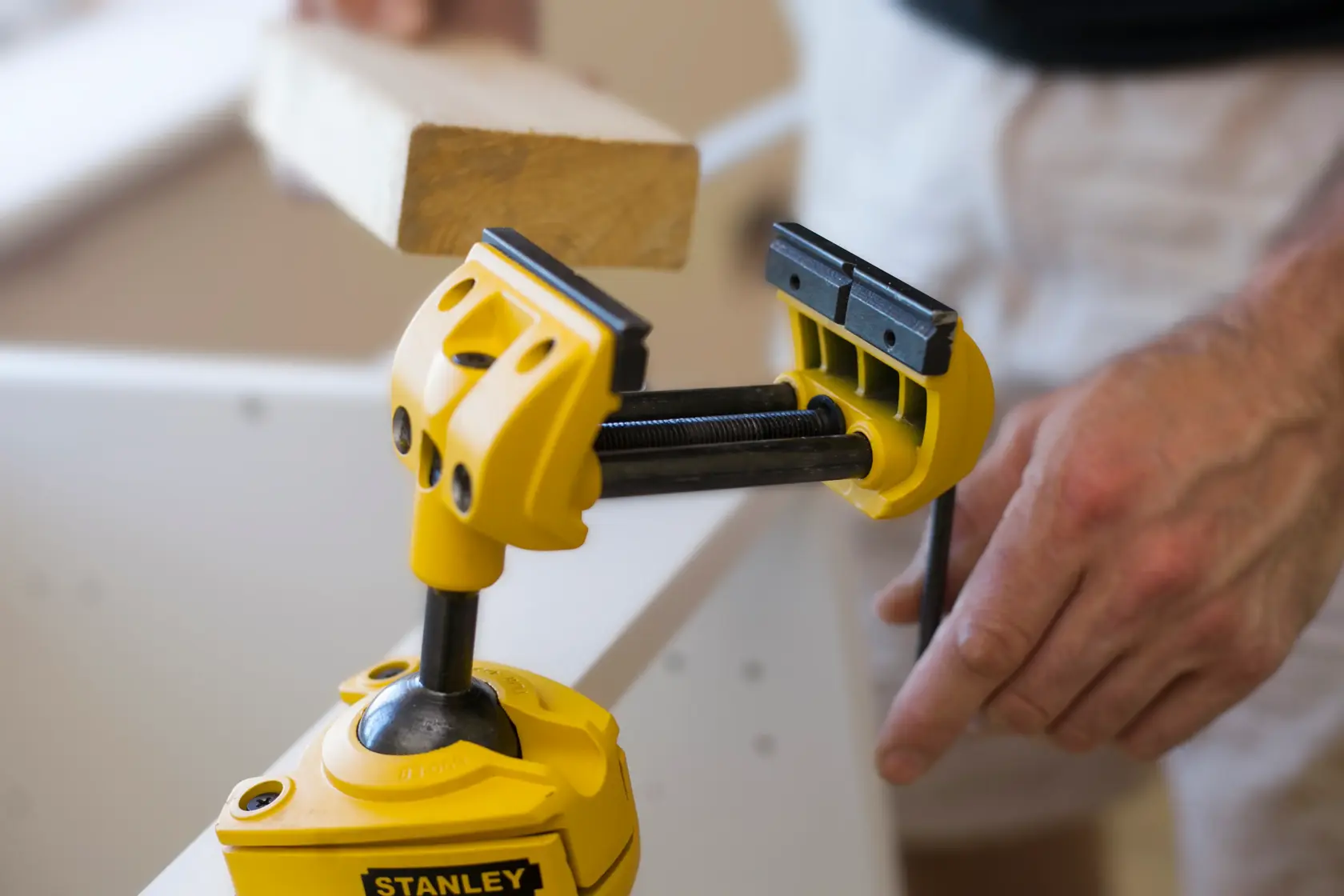 Stanley 1-83-069 adjustable yellow vise clamp holding wood, used in carpentry, close-up photography.