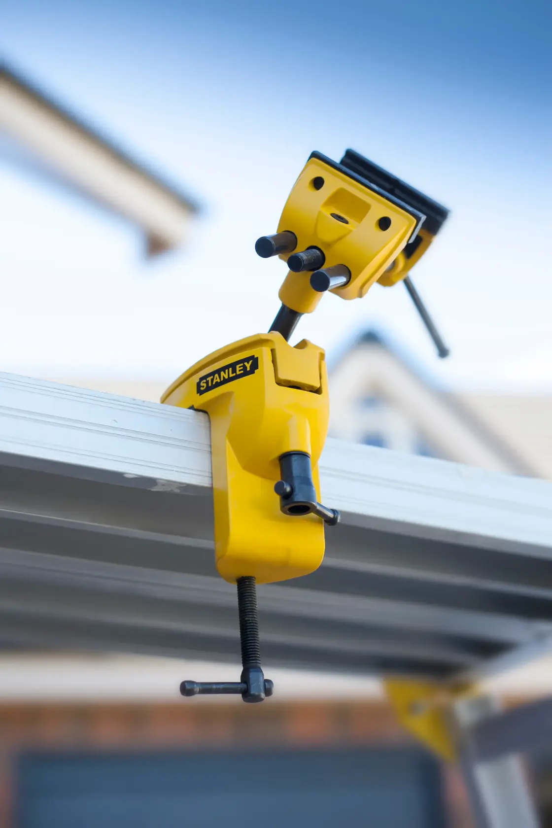 STANLEY 1-83-069 adjustable yellow metal vise clamped to a workbench, side angle outdoor photo.