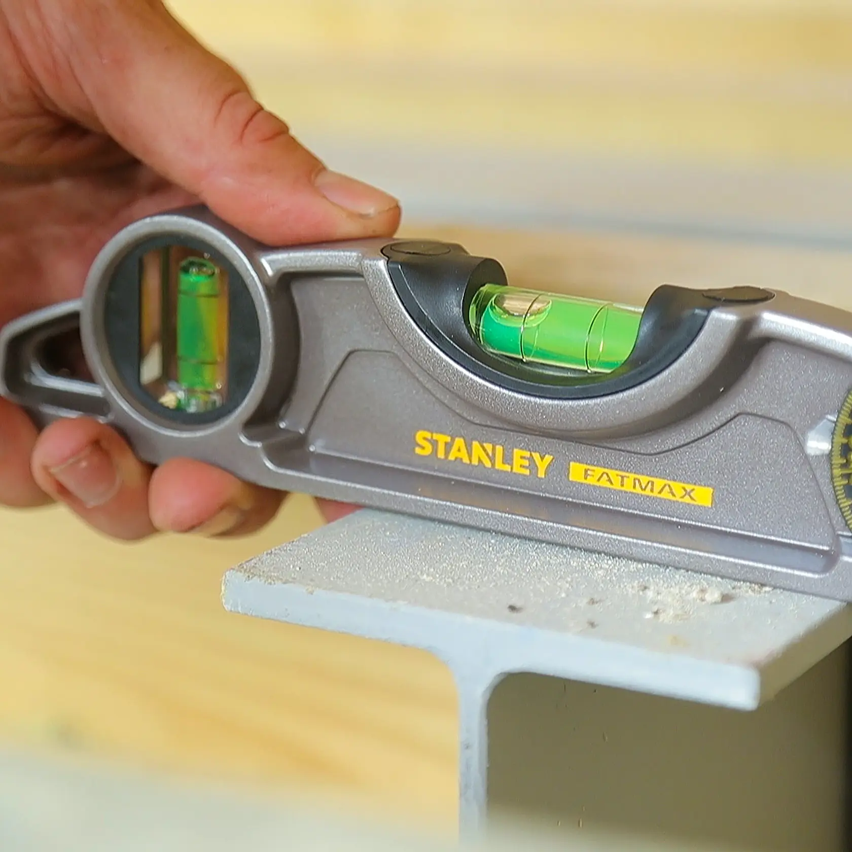 STANLEY 43-609I spirit level held by hand, photographed on steel beam, gray body with yellow branding.