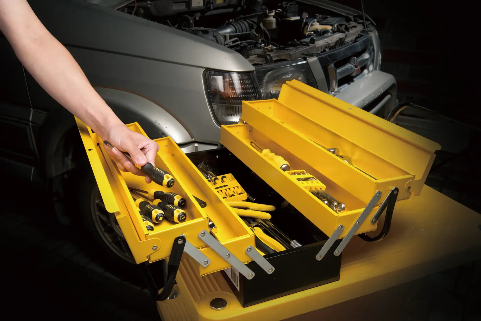 STANLEY 94738L yellow metal toolbox open on a workbench, filled with hand tools, person selecting a screwdriver.