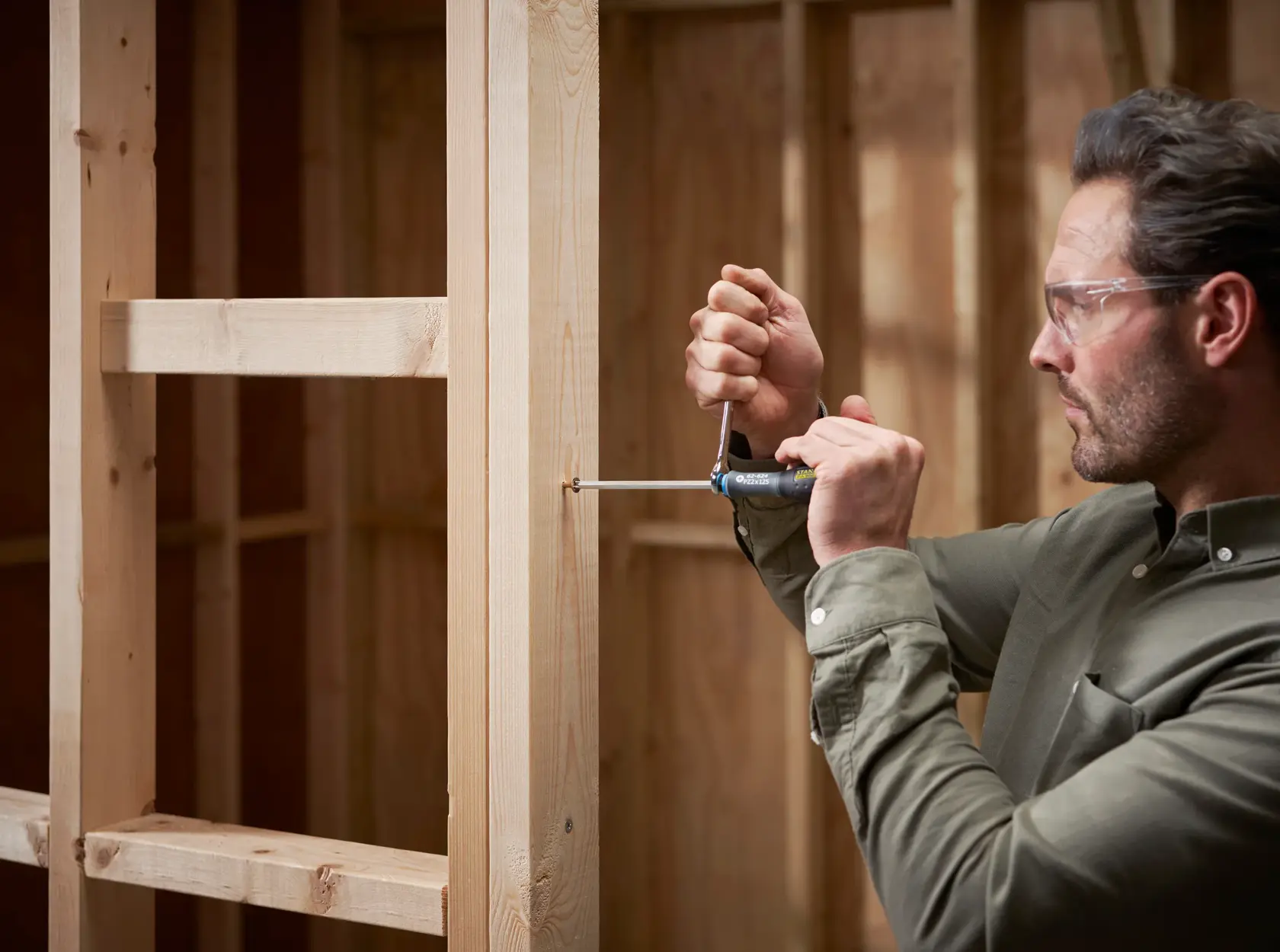 Photo of a person using a STANLEY FMHT0-62624 screwdriver on a wooden frame, construction setting.