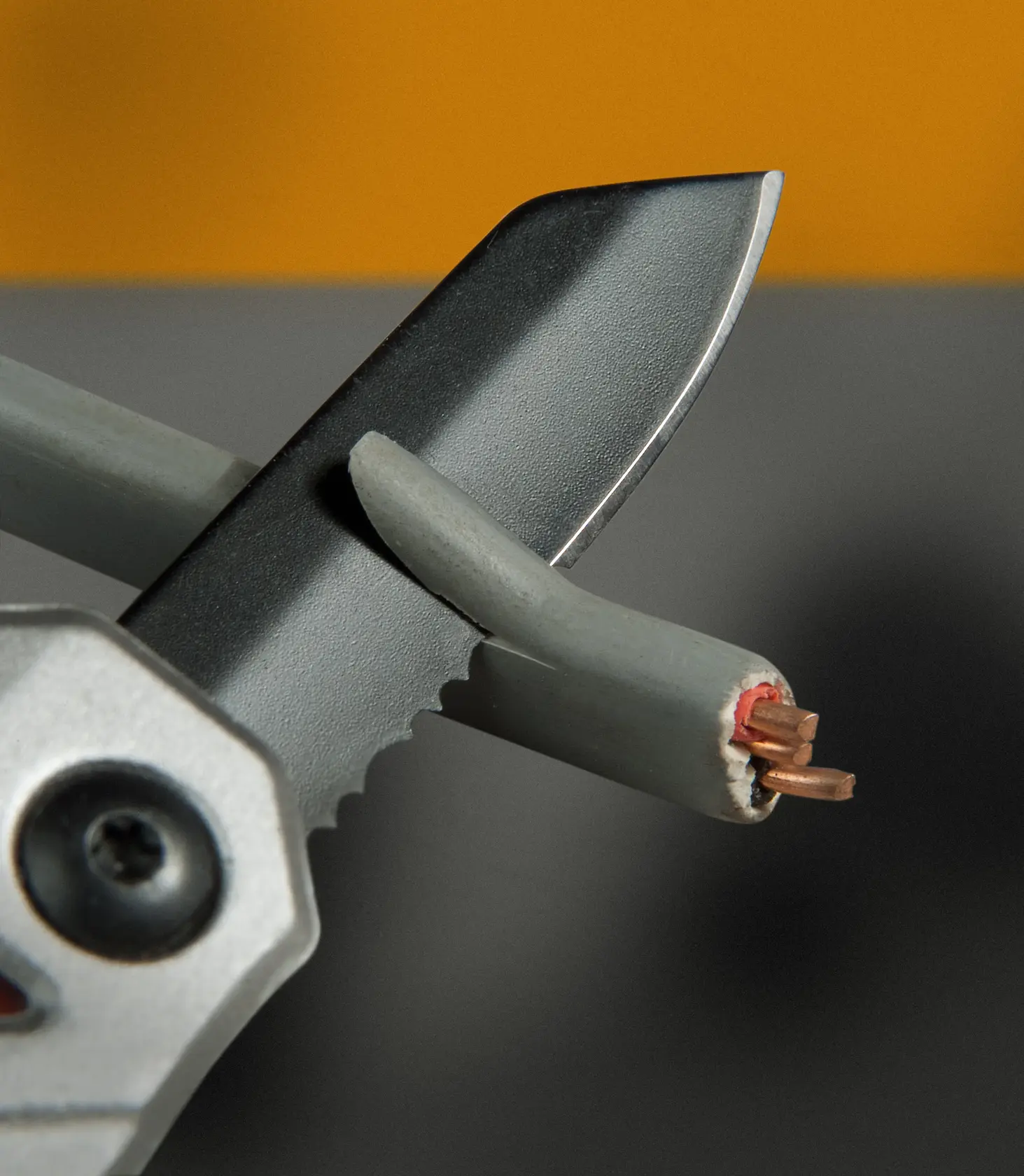 STANLEY FMHT0-72414 serrated blade cutting a grey electrical wire, close-up view.