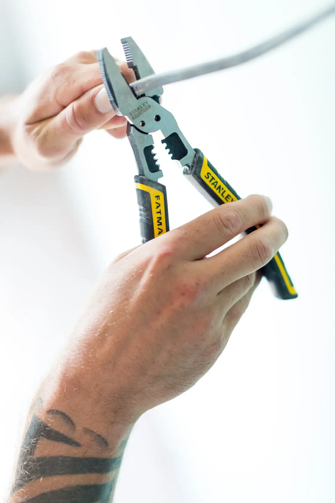 Photo of STANLEY FMHT0-75469 adjustable pliers with yellow and black handles in use, gripping a metal rod.