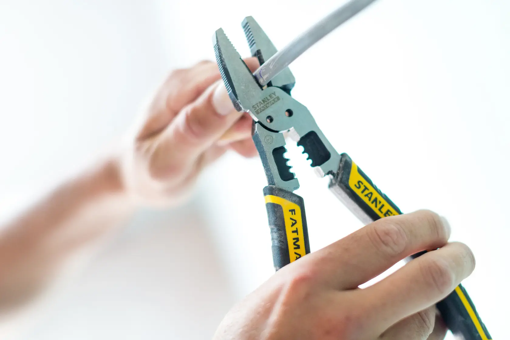 STANLEY FMHT0-75469 pliers gripping wire, close-up photography, black and yellow FATMAX handles.