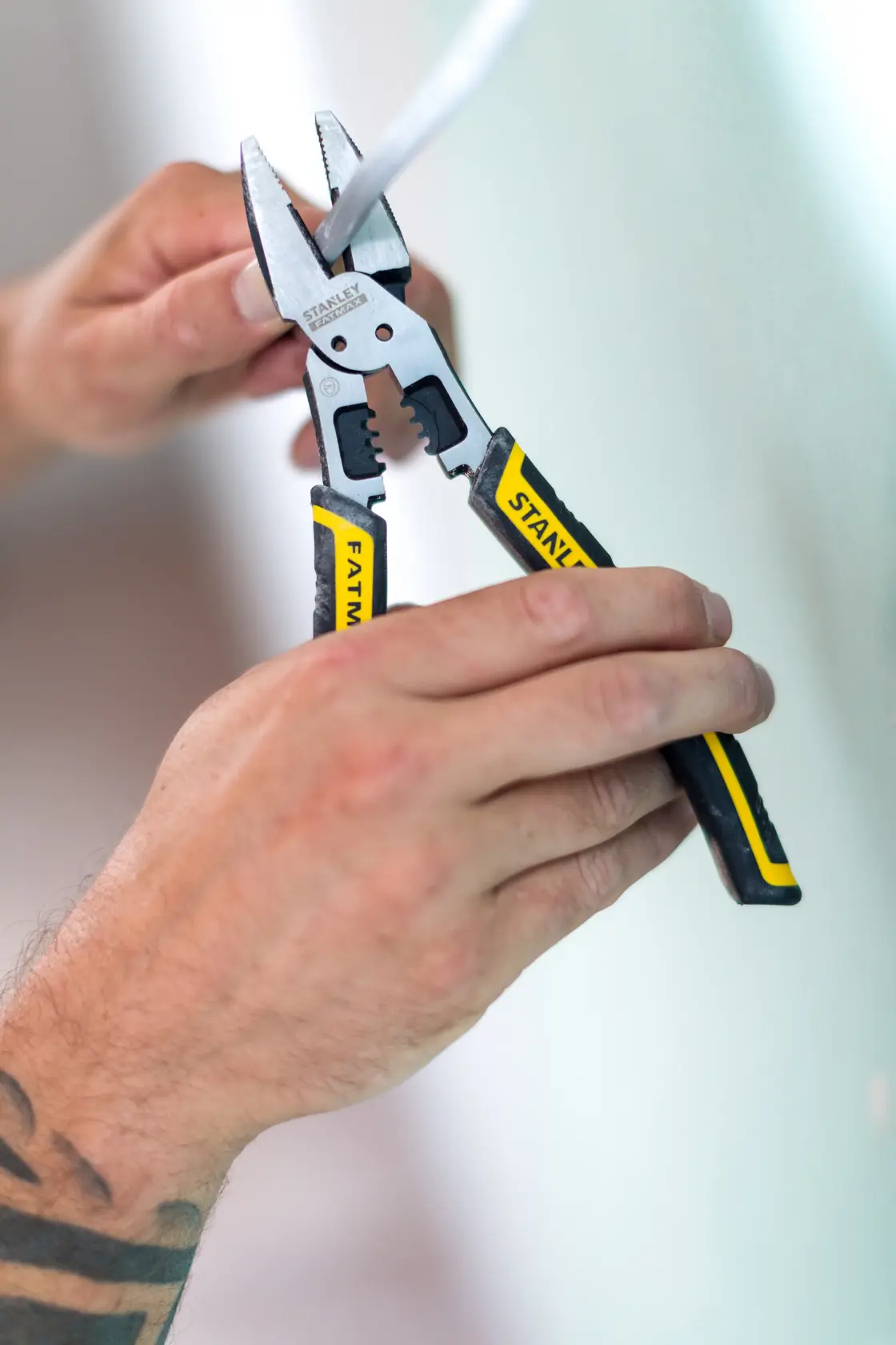 STANLEY FMHT0-75469 wire stripper pliers with black and yellow handles, shown stripping cable in hand, side view.