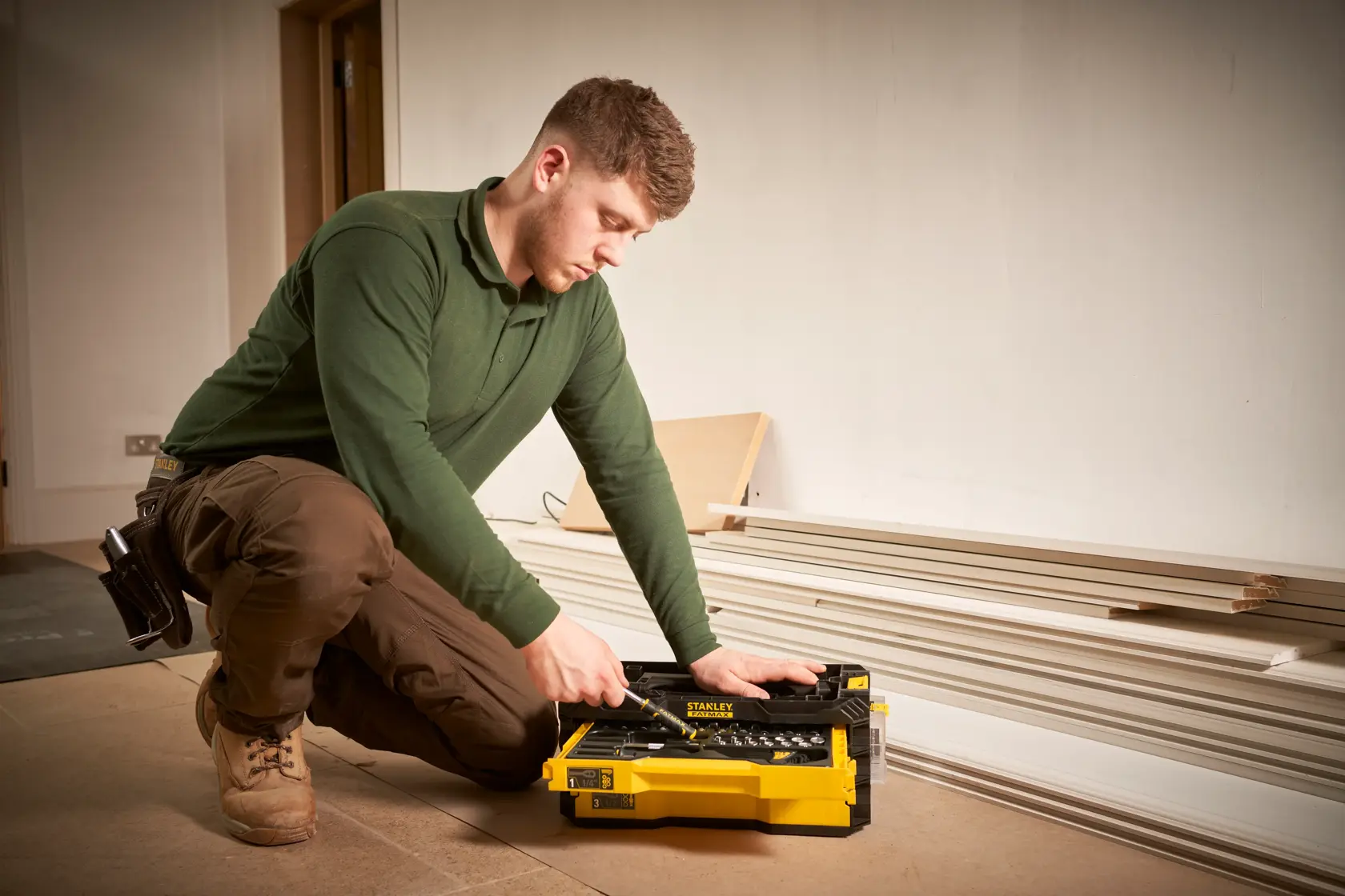 Photo of STANLEY FMMT98107-1 yellow tool box with hand tools, used by a worker kneeling indoors.