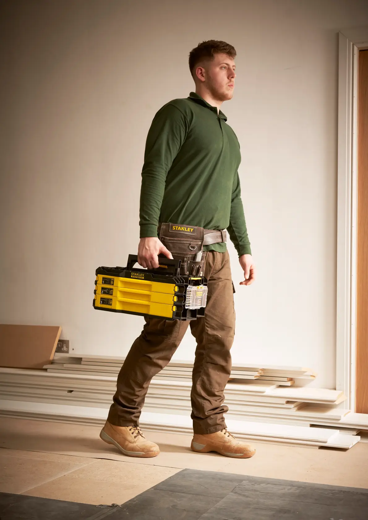 STANLEY FMMT98107-1 tool storage box, yellow and black, carried by worker in construction setting.