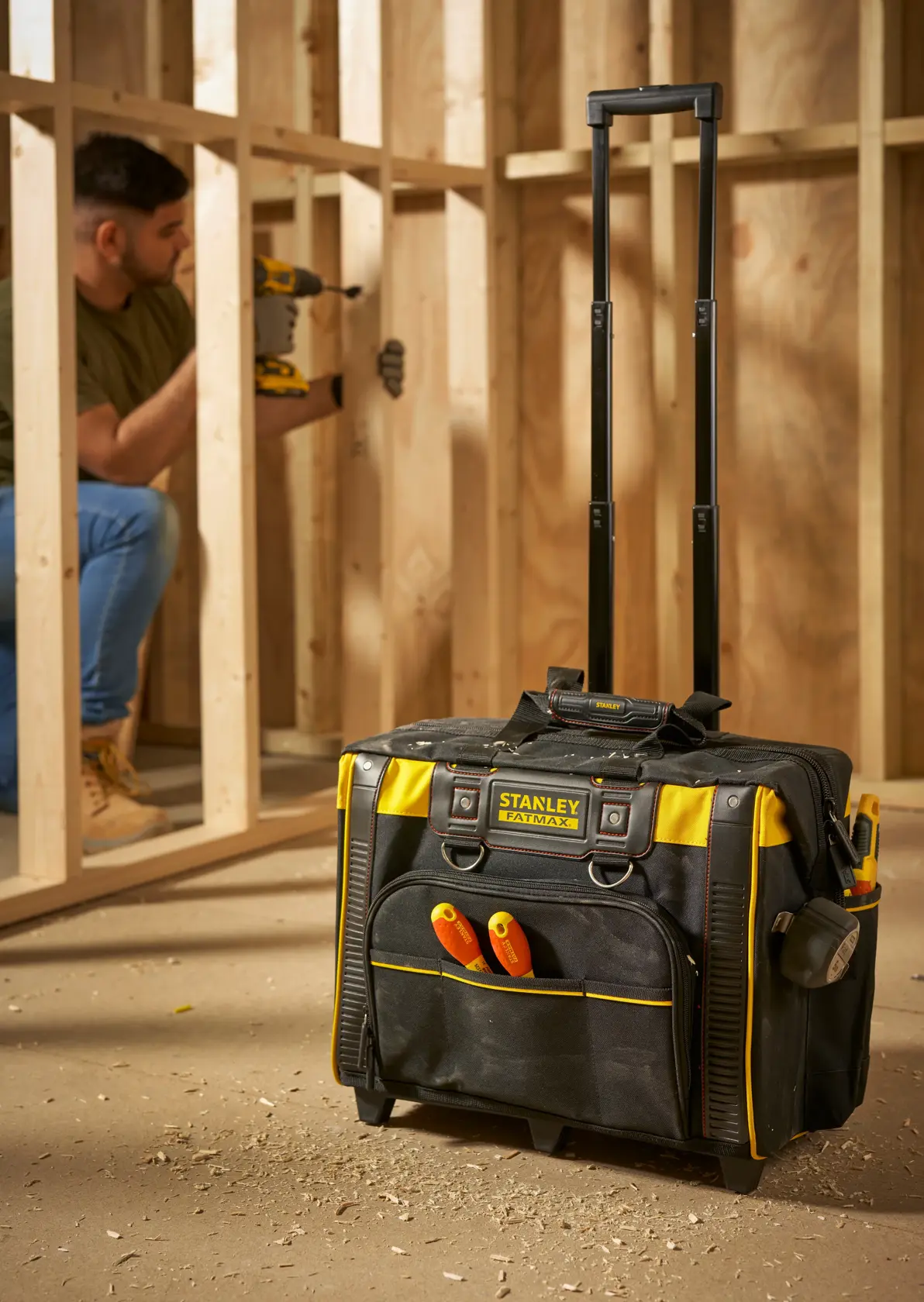 STANLEY FMST1-80148 rolling tool bag with handle, black and yellow, at construction site, front angle.