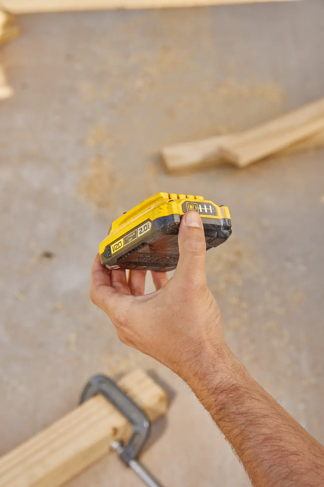 Photography of STANLEY SB202 V20 2.0Ah battery held in hand at a woodworking workspace.
