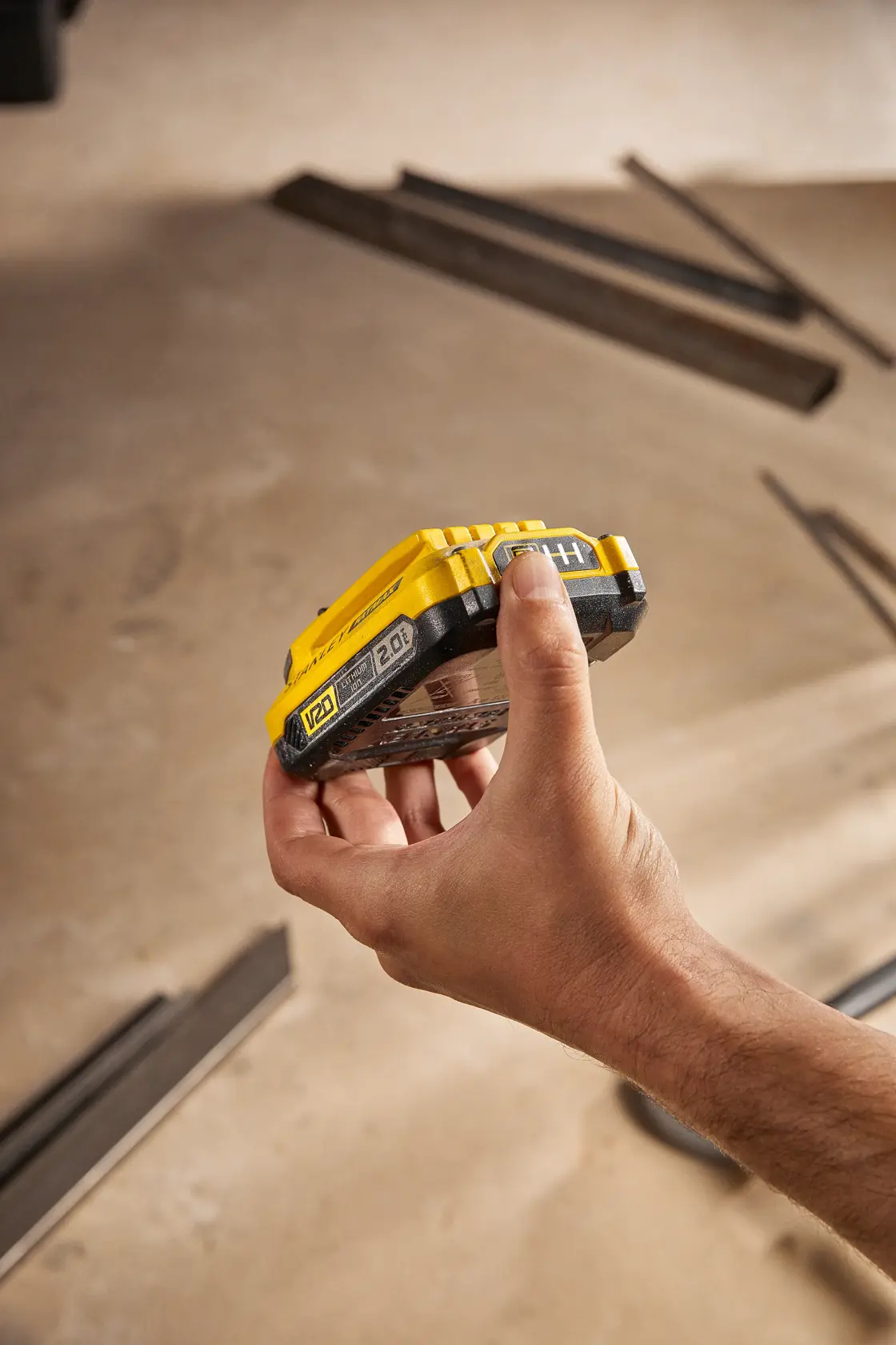STANLEY SB202 battery held in hand, yellow and black, V20 series, shown in workshop setting.