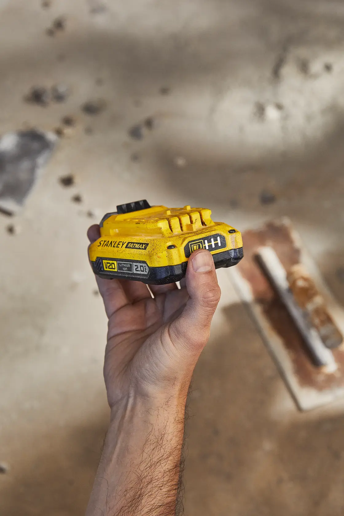 Stanley SB202 battery held in hand, yellow V20 lithium-ion, photography on construction site.