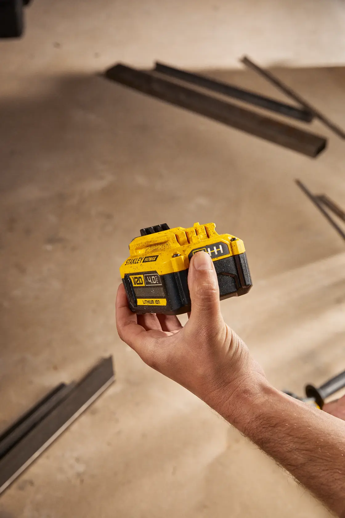 Photo of STANLEY SB204-KR 20V lithium-ion battery held in a hand, construction materials in background.