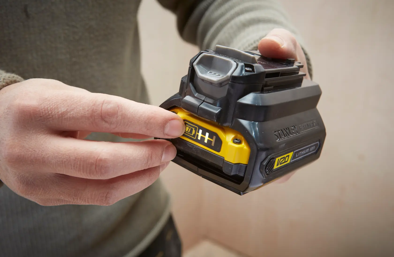 Photo of STANLEY SBA100 V20 lithium-ion battery held in hand, showing yellow label and black casing.