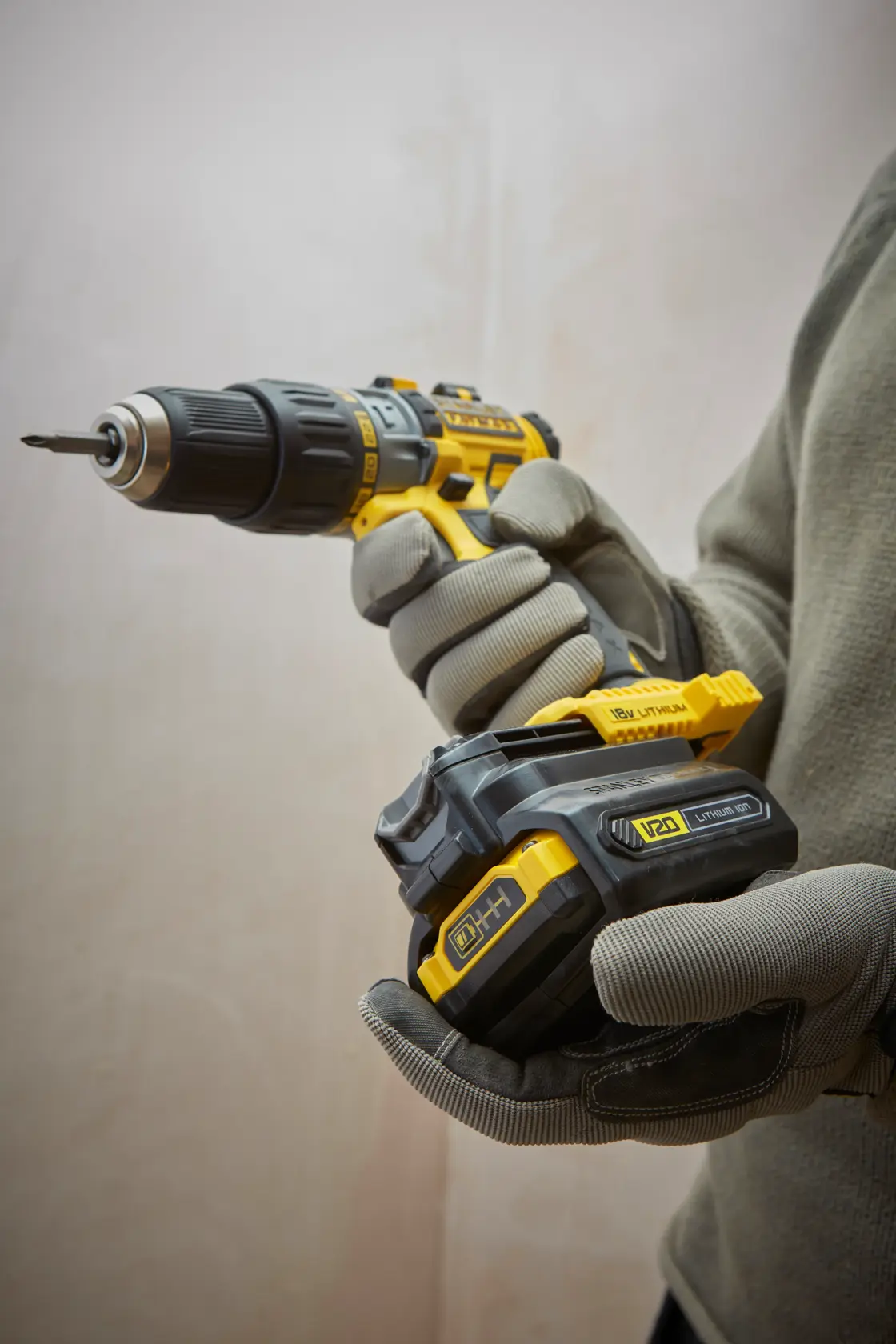 STANLEY SBA100 cordless drill held in gloved hands, yellow and black, side angle, photography product.