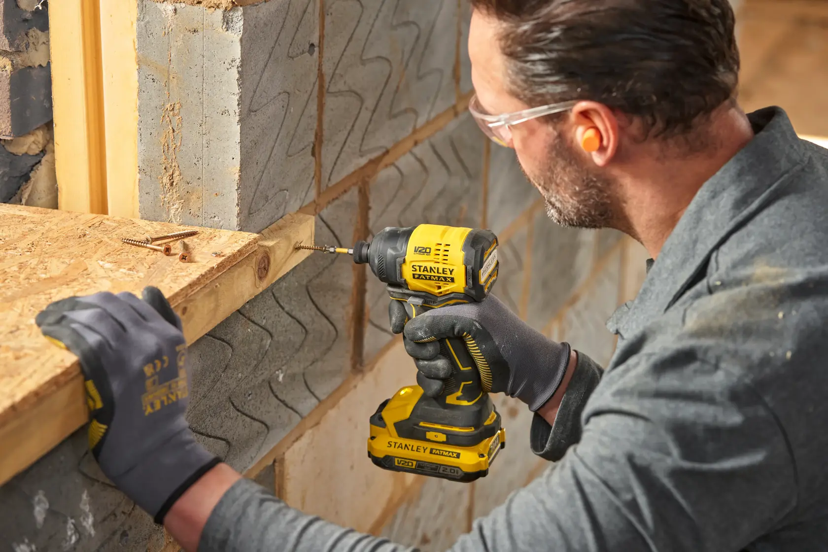 STANLEY SBI811 impact driver in use, yellow and black, drilling into wood near a concrete wall.