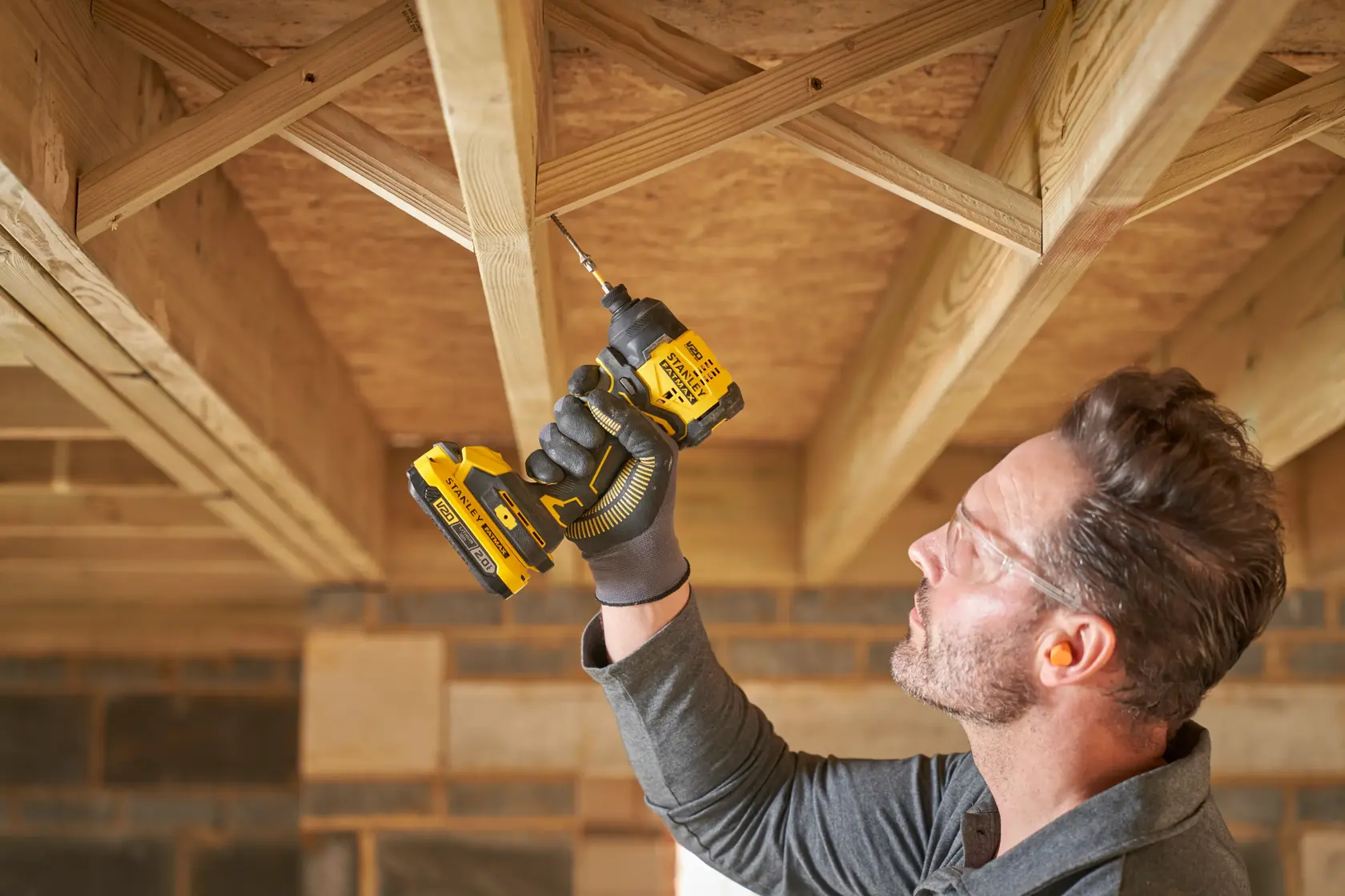 STANLEY SBI811 cordless drill in use on ceiling wood beams, shown in a construction setting.