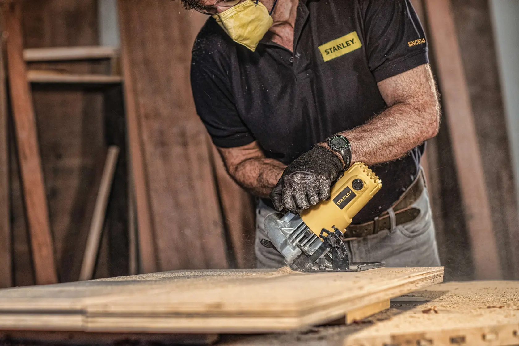 STANLEY SC16 circular saw cutting wood, photography of user wearing gloves and mask in workshop.