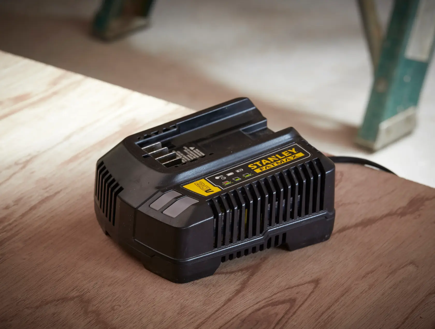 Stanley SC200 battery charger, black with yellow label, angled on wooden surface in workshop.