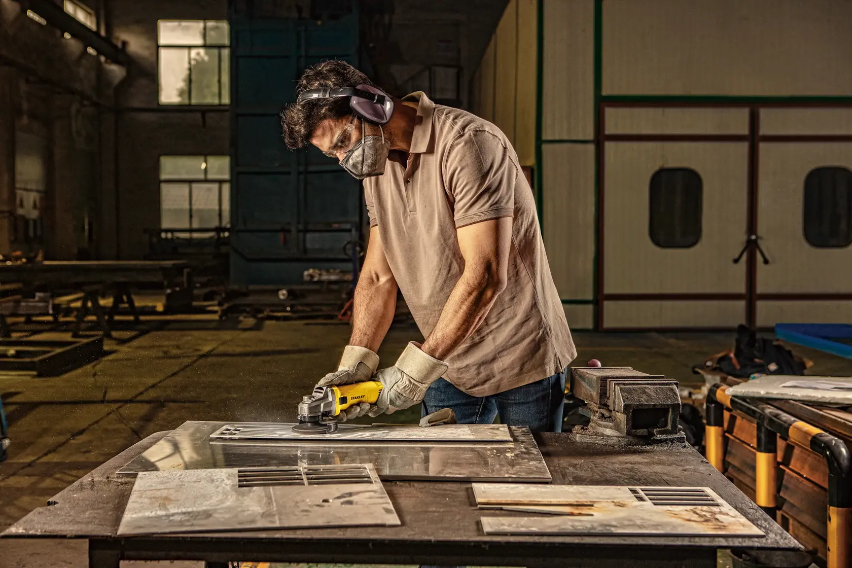 Stanley SG6100 worker using grinder on metal in workshop, side angle, safety gear worn.