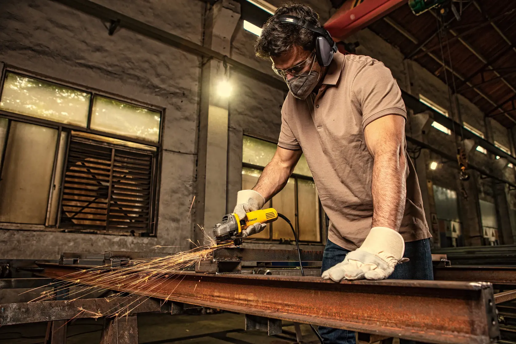 STANLEY SG6100 angle grinder in use on metal beam, sparks flying, indoor workshop setting.