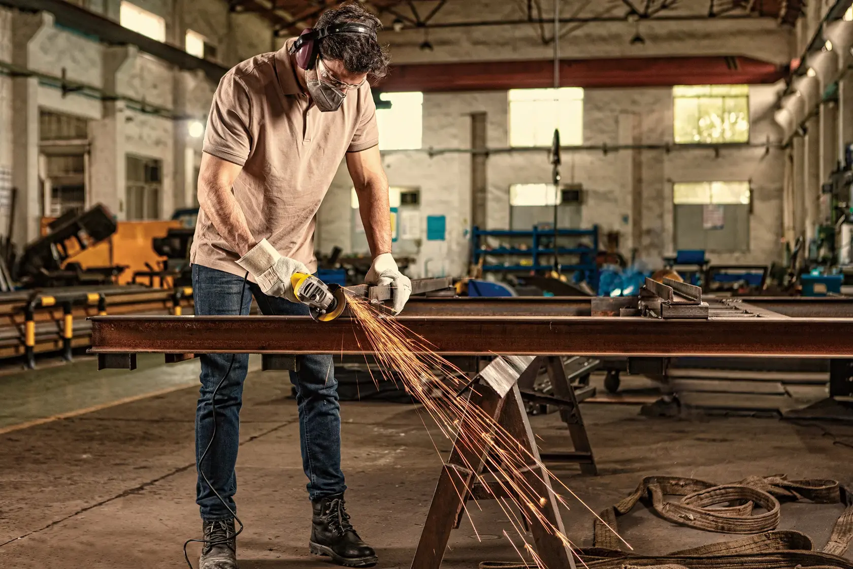 STANLEY SG7100 angle grinder used on metal beam in workshop, sparks flying, worker wearing safety gear.