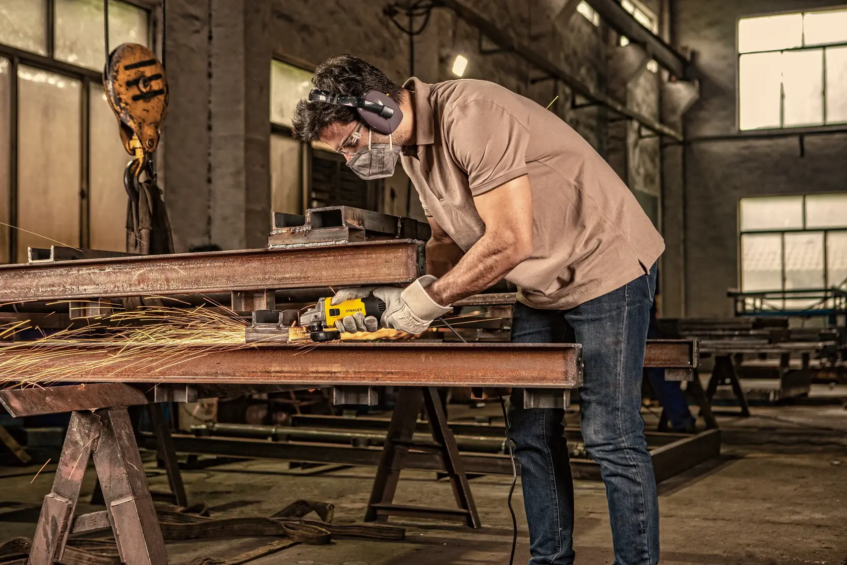 Stanley SG7100 angle grinder in use on steel beams in industrial workshop, side view.