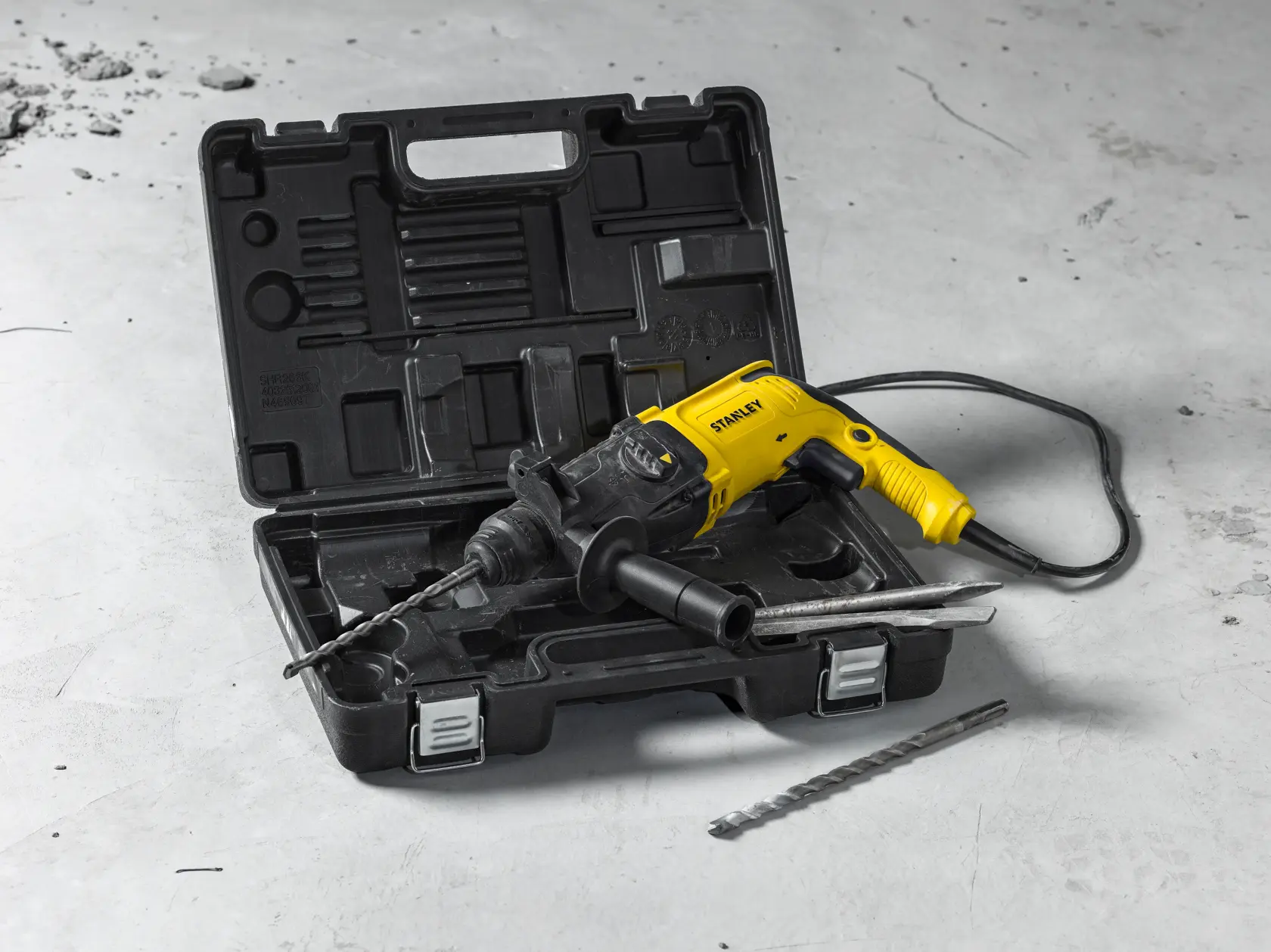 STANLEY SHR263K-BR rotary hammer drill with yellow and black body, carrying case, and accessories displayed on concrete.