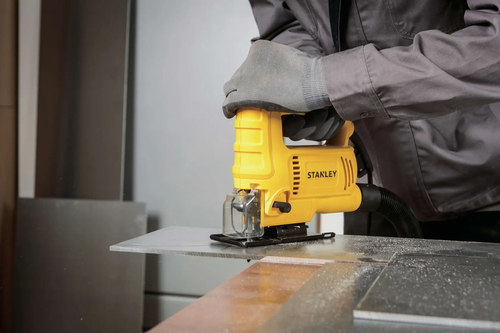 Stanley SJ60 jigsaw cutting metal sheet, yellow tool held with gloves, photo in workshop.