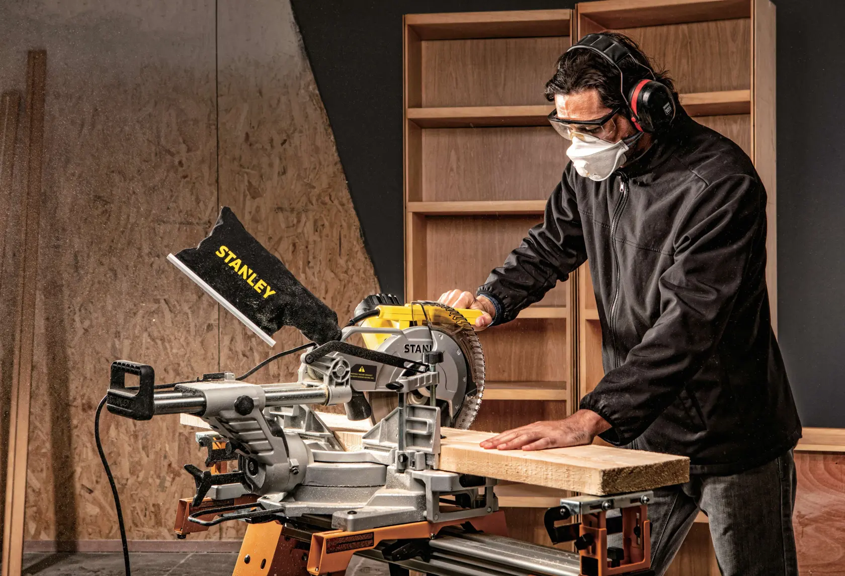 Photo of STANLEY SM18-B2C compound miter saw in use, cutting wood on a workbench in a workshop setting.
