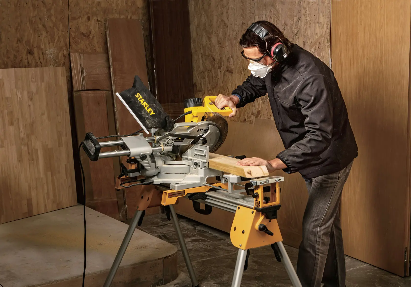 STANLEY SM18-B2C miter saw in use, cutting wood in a workshop setting, operator wearing ear protection.