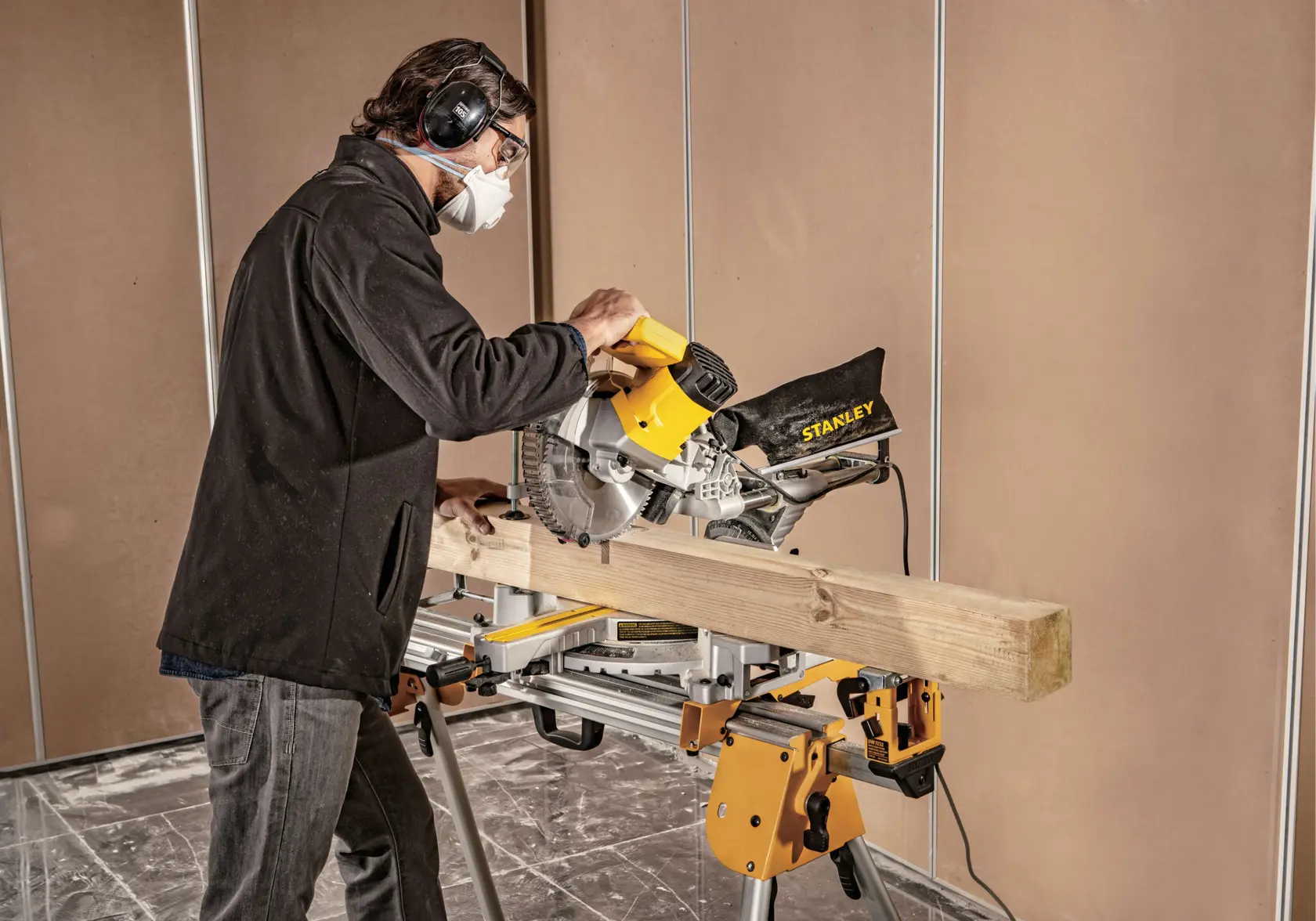 Photo of a person using a STANLEY SM18-B2C miter saw to cut a wooden beam indoors, wearing safety gear.