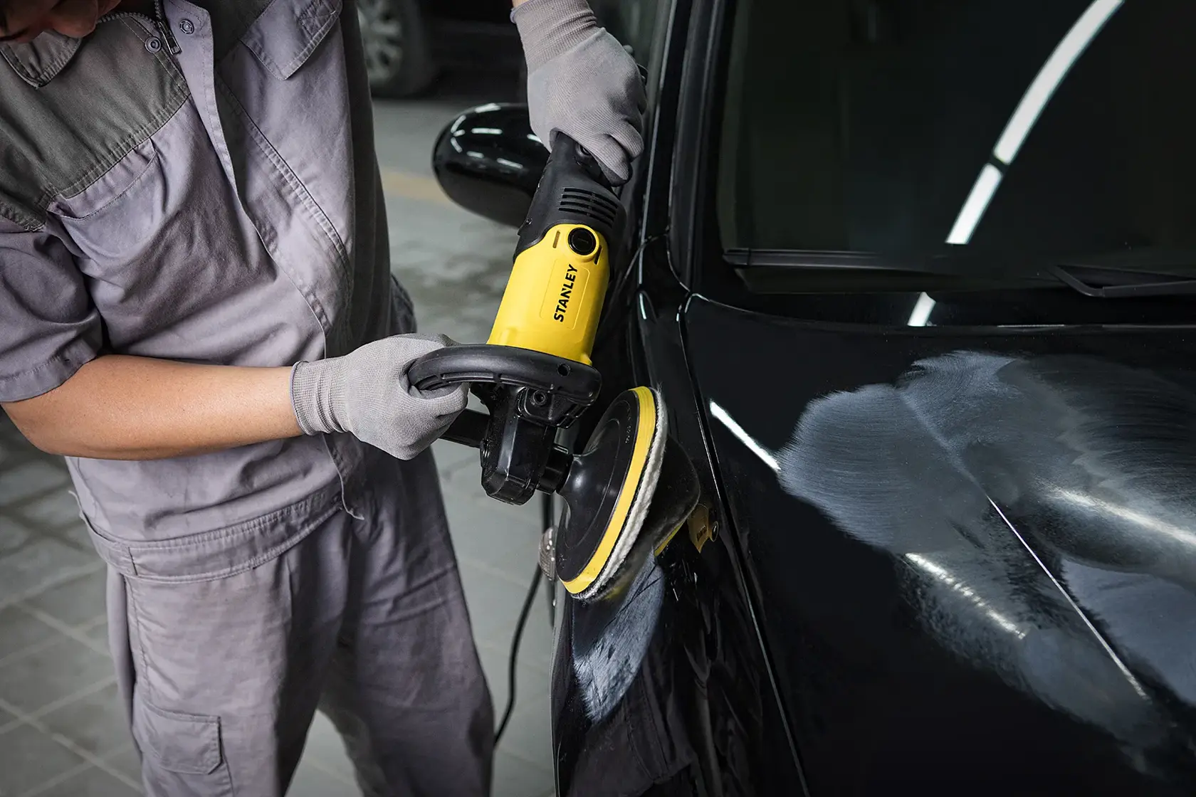 STANLEY SP137 yellow car polisher in use, close-up showing polishing of black vehicle hood.