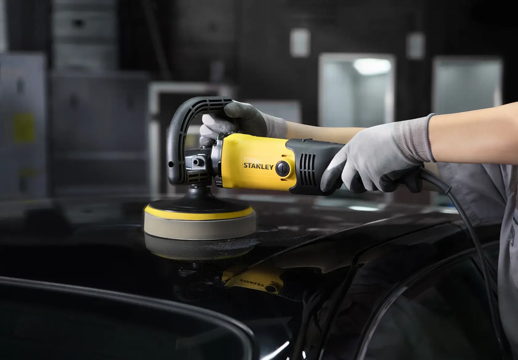 Stanley SP137 yellow and black polisher in use on car roof, held by gloved hands in workshop setting.